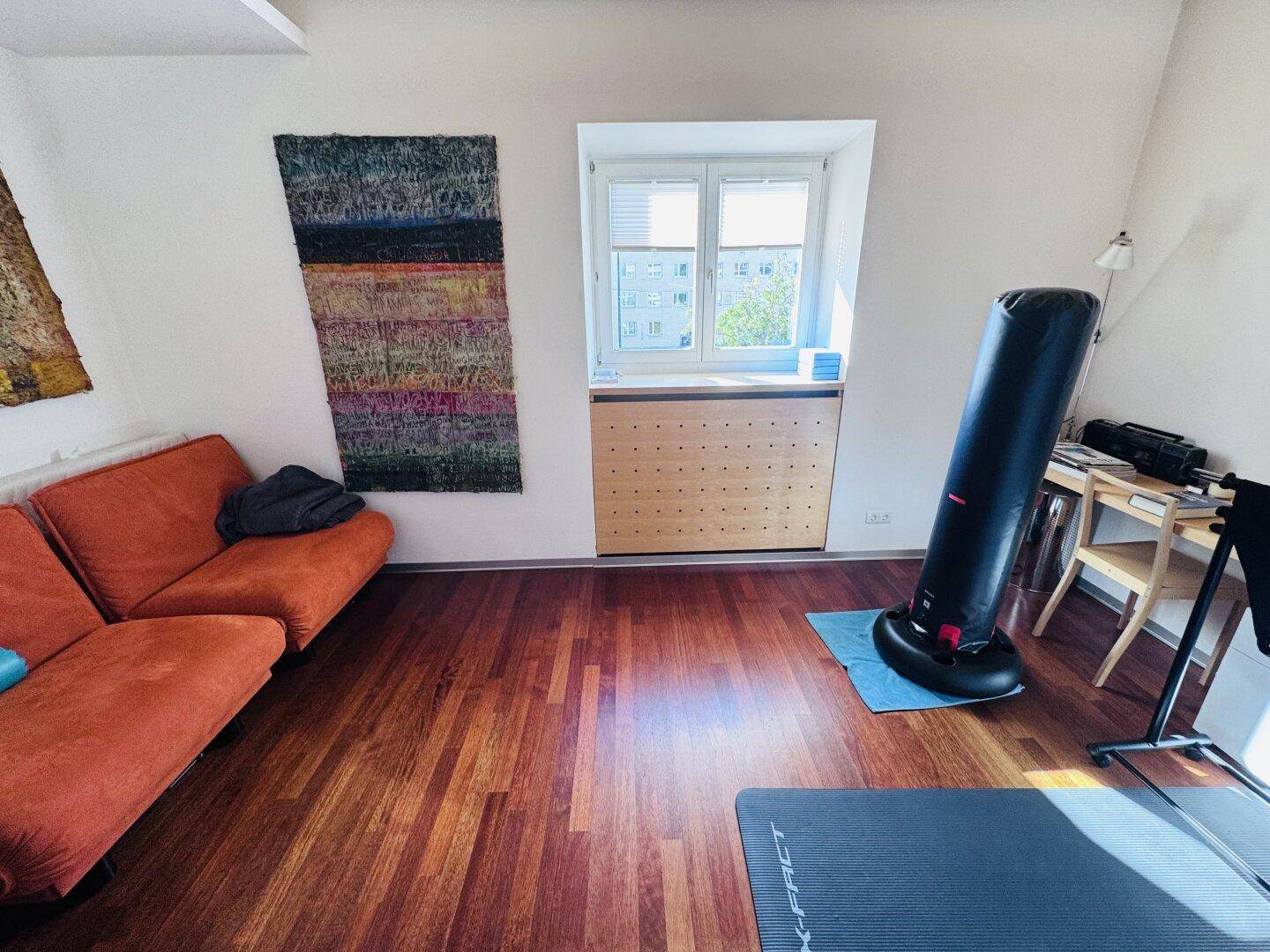 Ein Wohnbereich mit Holzboden, einem orangefarbenen Sofa und einem Fenster, das viel Licht hereinlässt.