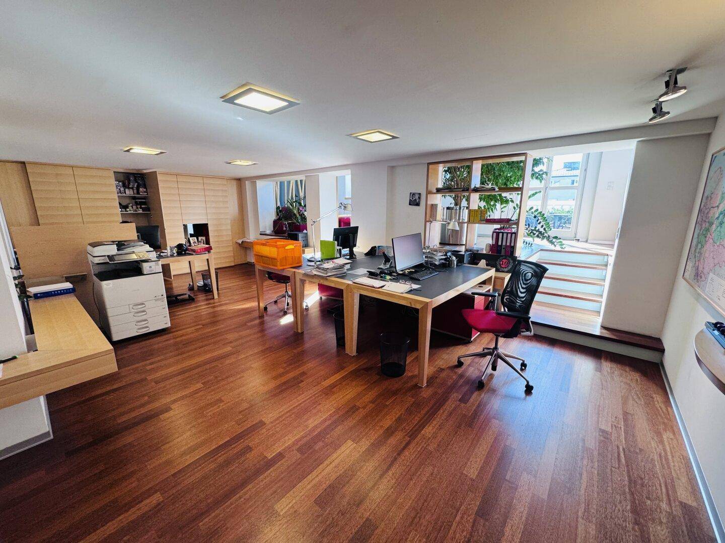 Ein großes, offenes Büro mit Holzboden, mehreren Arbeitsplätzen und viel natürlichem Licht.