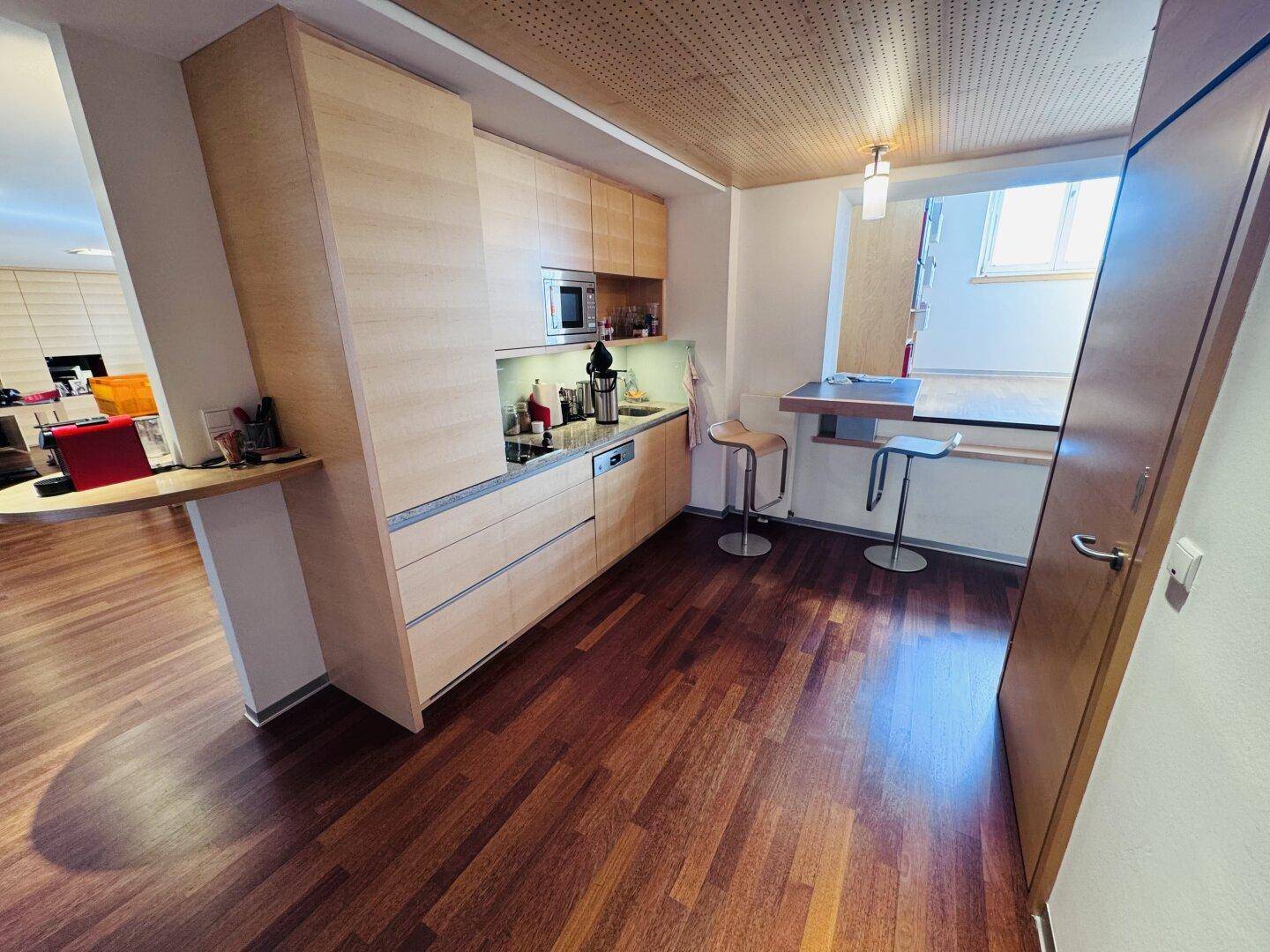 Eine moderne Küchenzeile mit Holzelementen, integrierten Geräten und einem kleinen Bartresen.