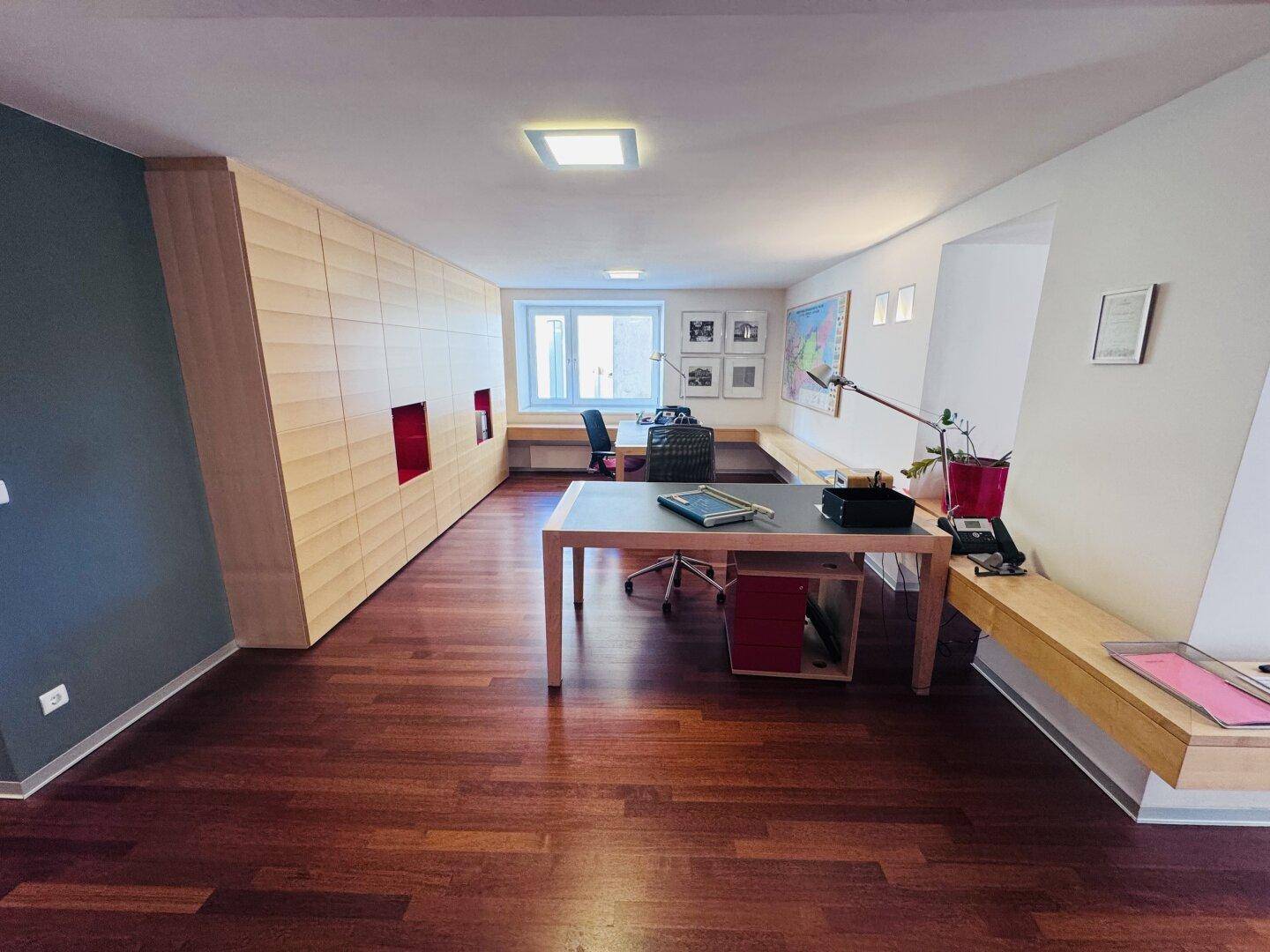 Ein geräumiges Büro mit Holzboden, einer langen Schrankwand und einem großen Schreibtisch.