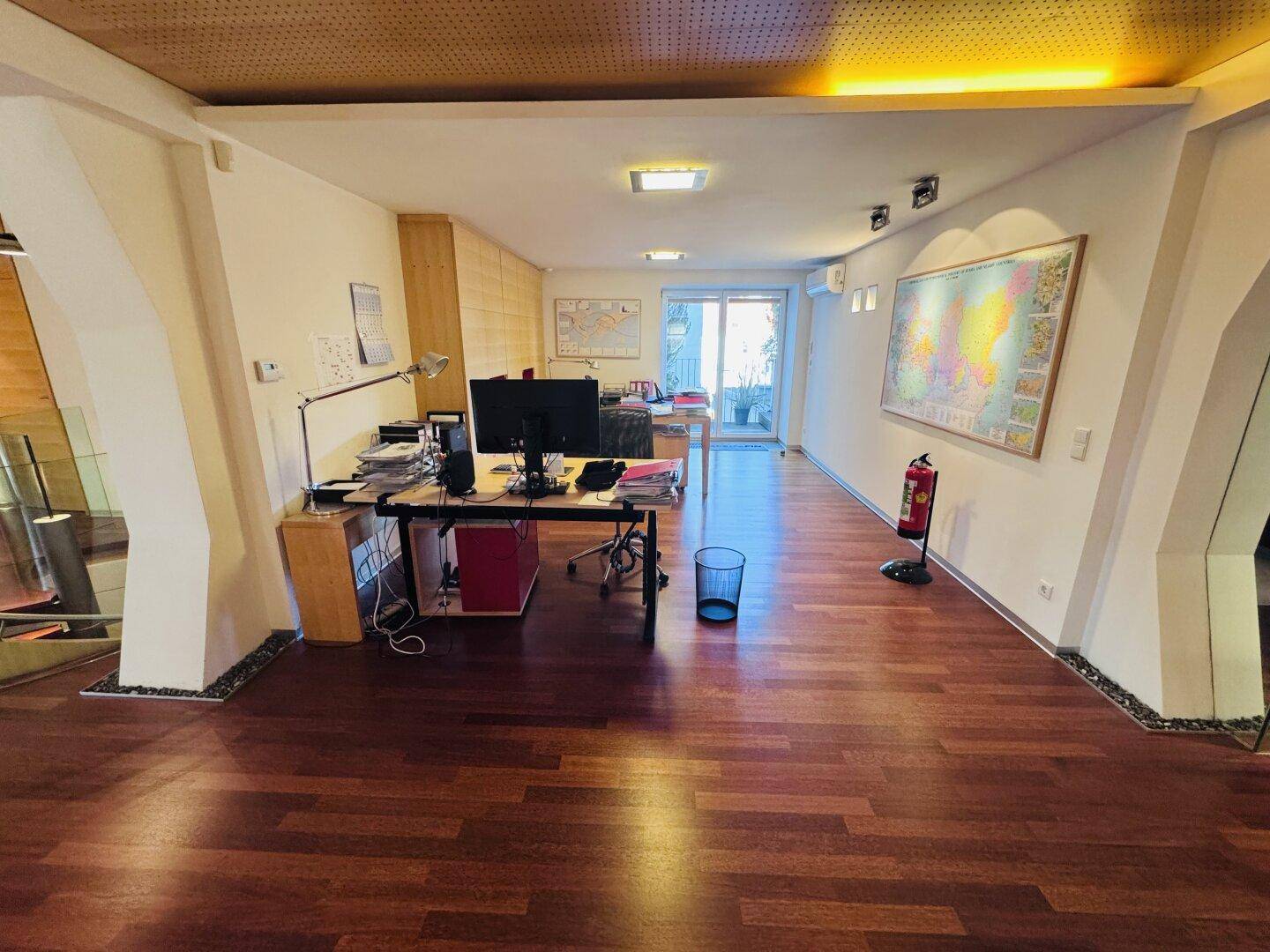 Ein offenes Büro mit Holzboden, mehreren Arbeitsplätzen und einem Ausgang zu einem Außenbereich.
