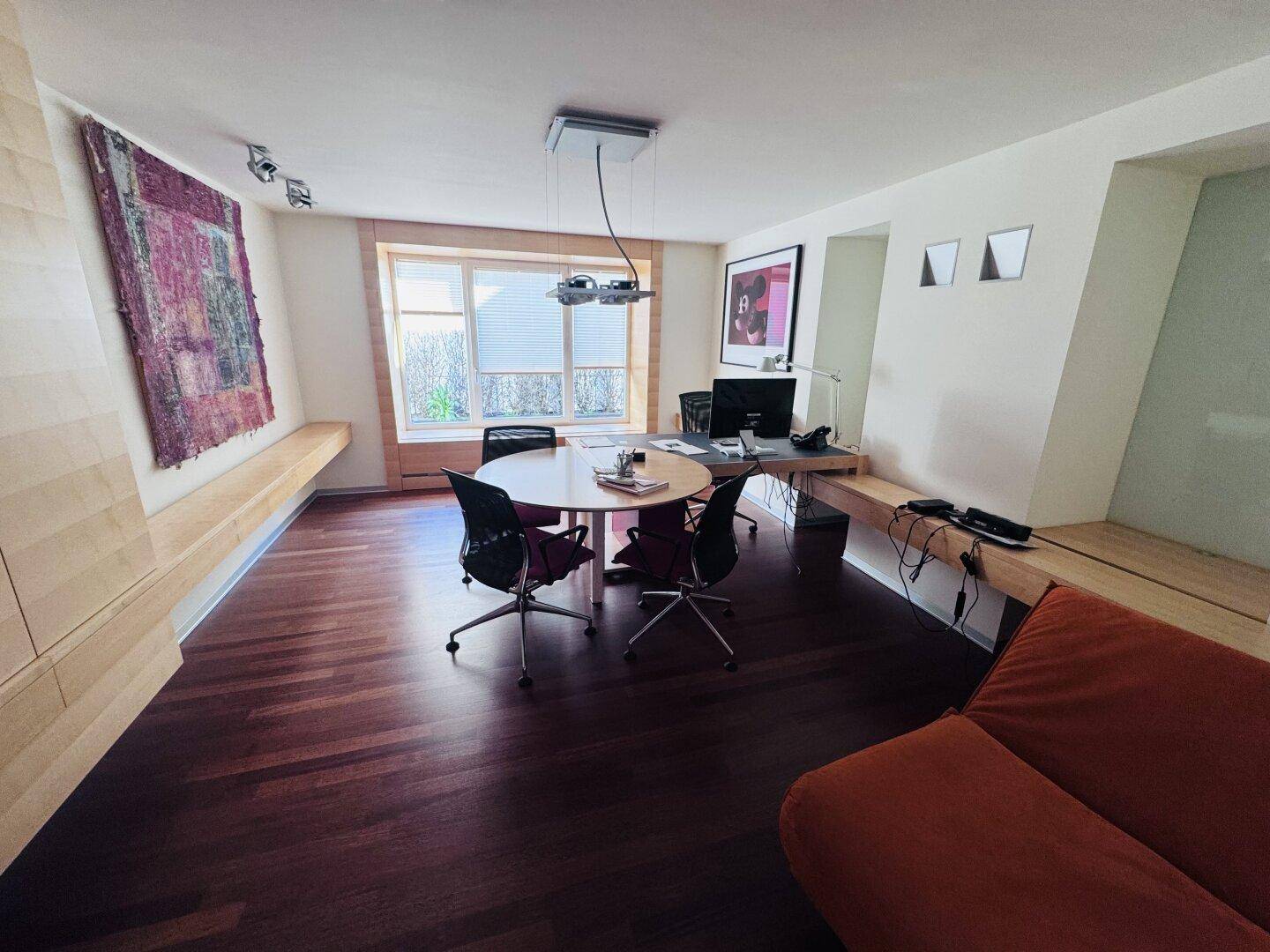 Ein vielseitiger Raum mit Holzboden, einem runden Besprechungstisch und einem Sofa, ideal für Arbeit und Entspannung.