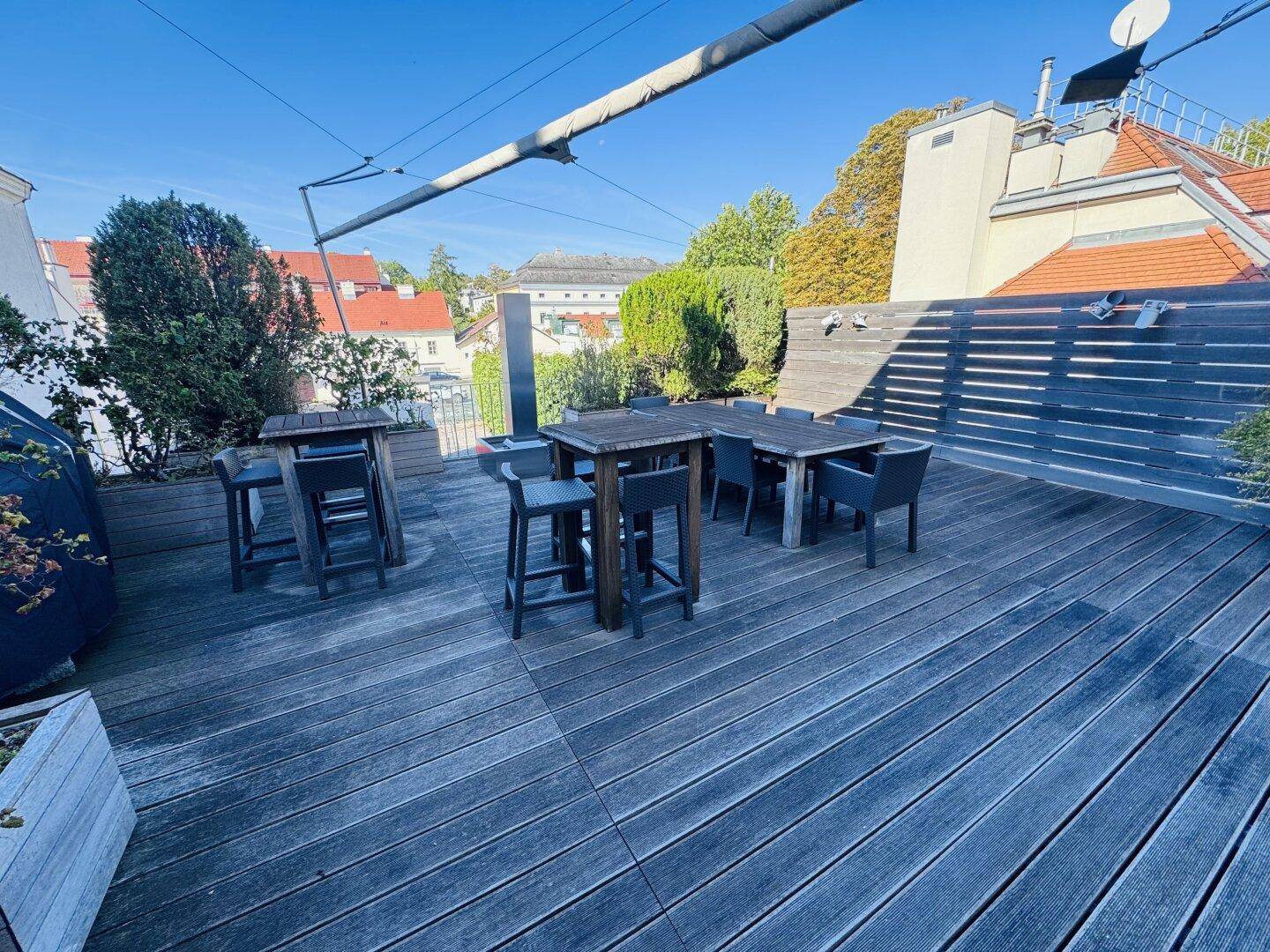Eine große Dachterrasse mit Holzdielen, verschiedenen Sitzbereichen und Blick auf die Umgebung.