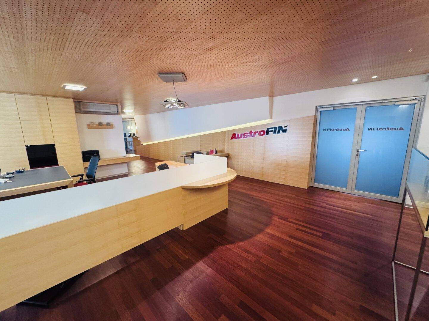 Moderner Bürobereich mit Holzfußboden, Holzdecke und Glastüren, die zu weiteren Räumen führen.