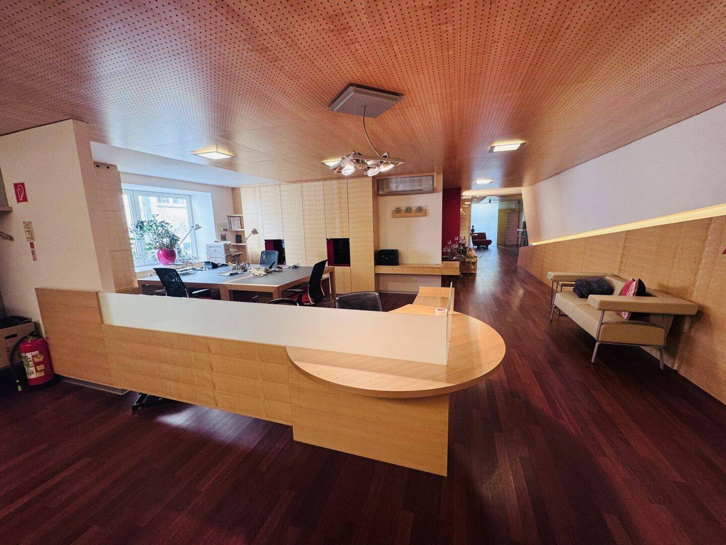 Empfangsbereich eines Büros mit Holzfußboden, Holzdecke und einer geschwungenen Rezeption.