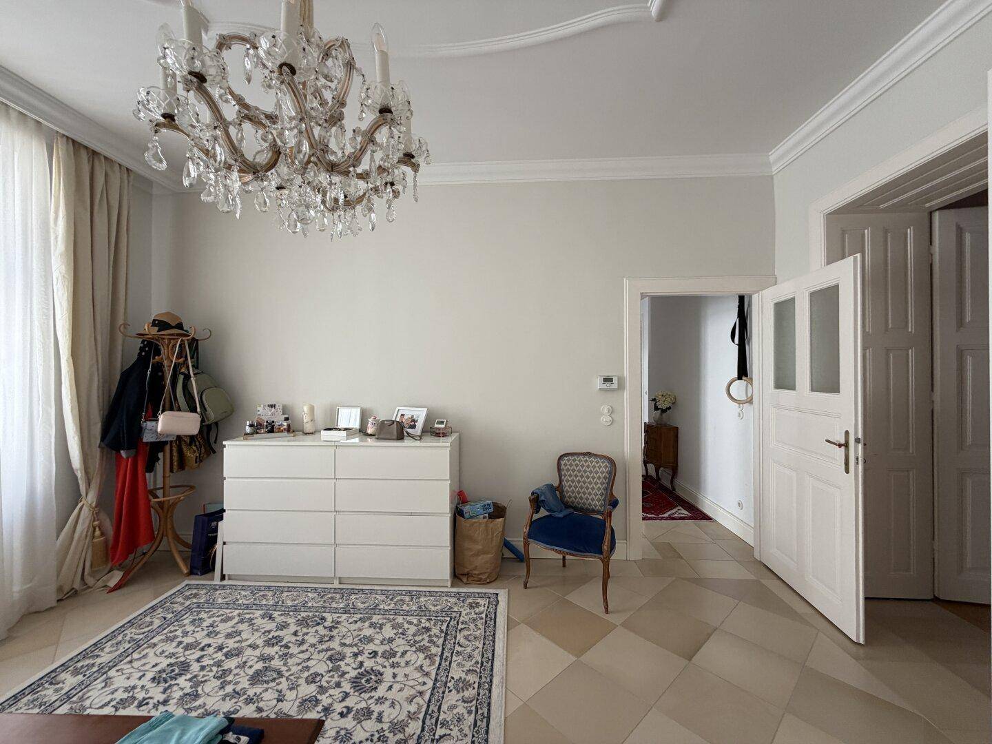 Schlafzimmer mit Kommode, Stuhl und Zugang zu einem weiteren Raum.