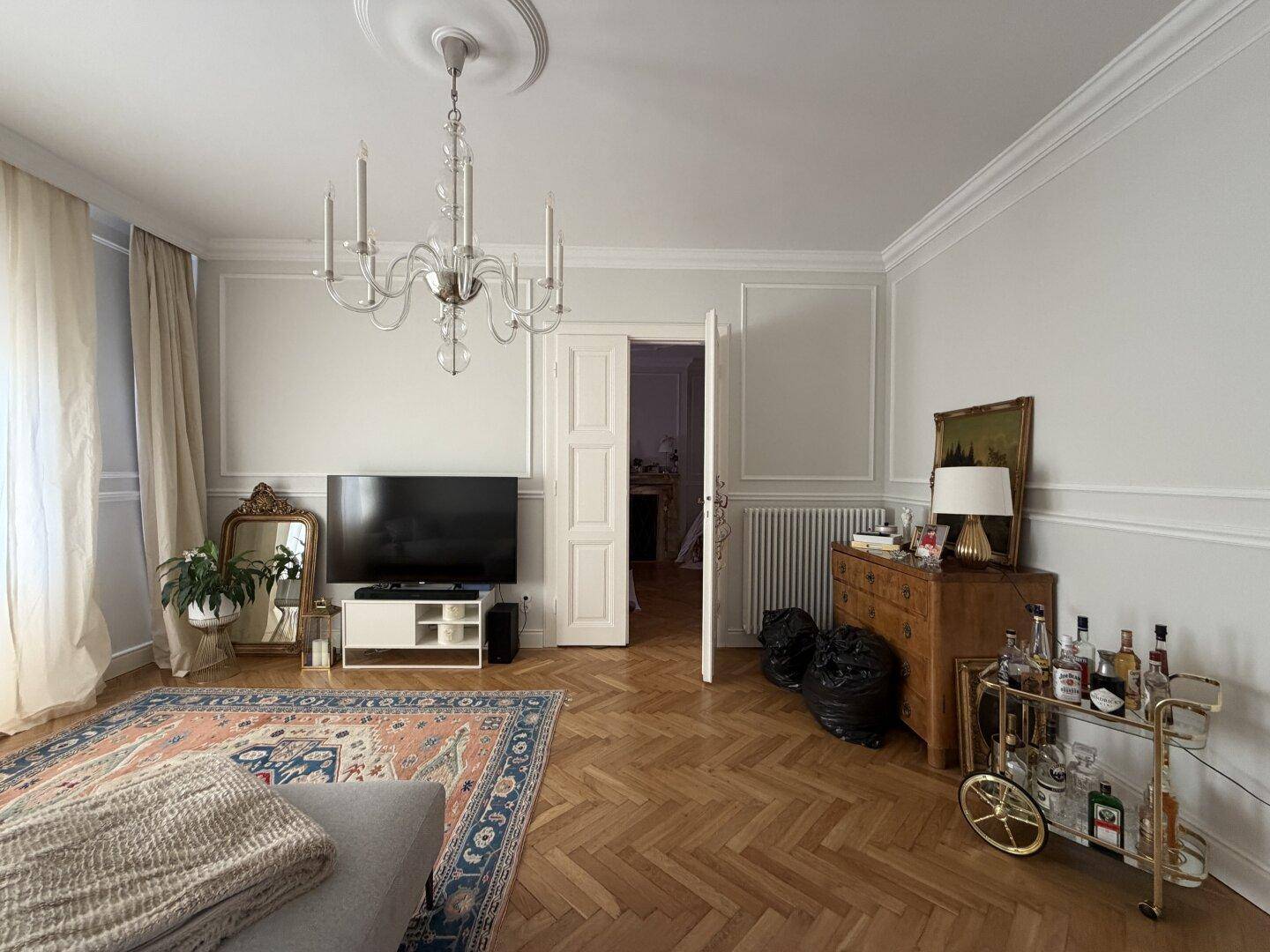 Elegantes Wohnzimmer mit Fischgrätparkett, Kronleuchter und dekorativem Kamin.