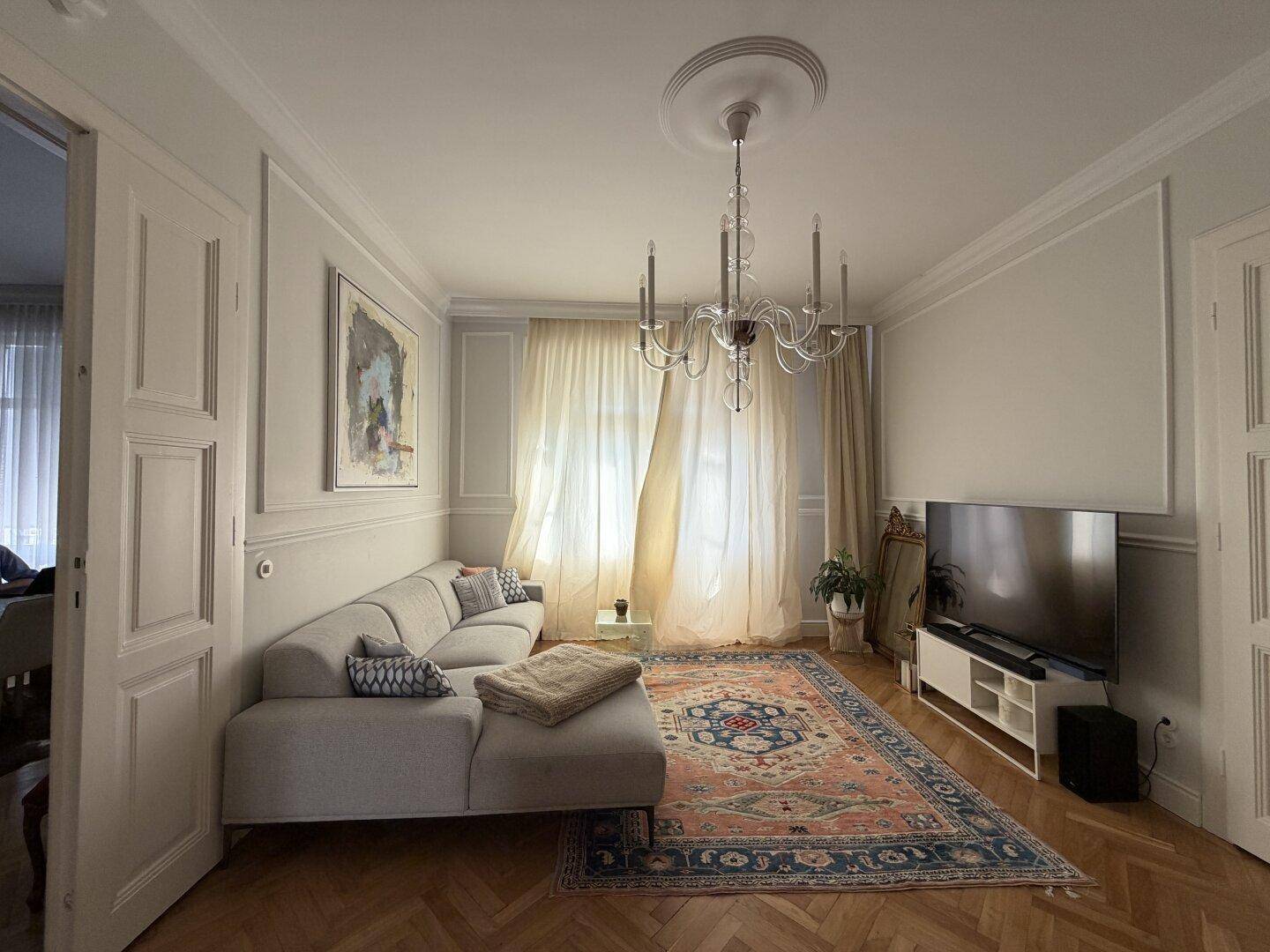 Helles Wohnzimmer mit bequemem Sofa, Parkettboden und stilvollem Kronleuchter.