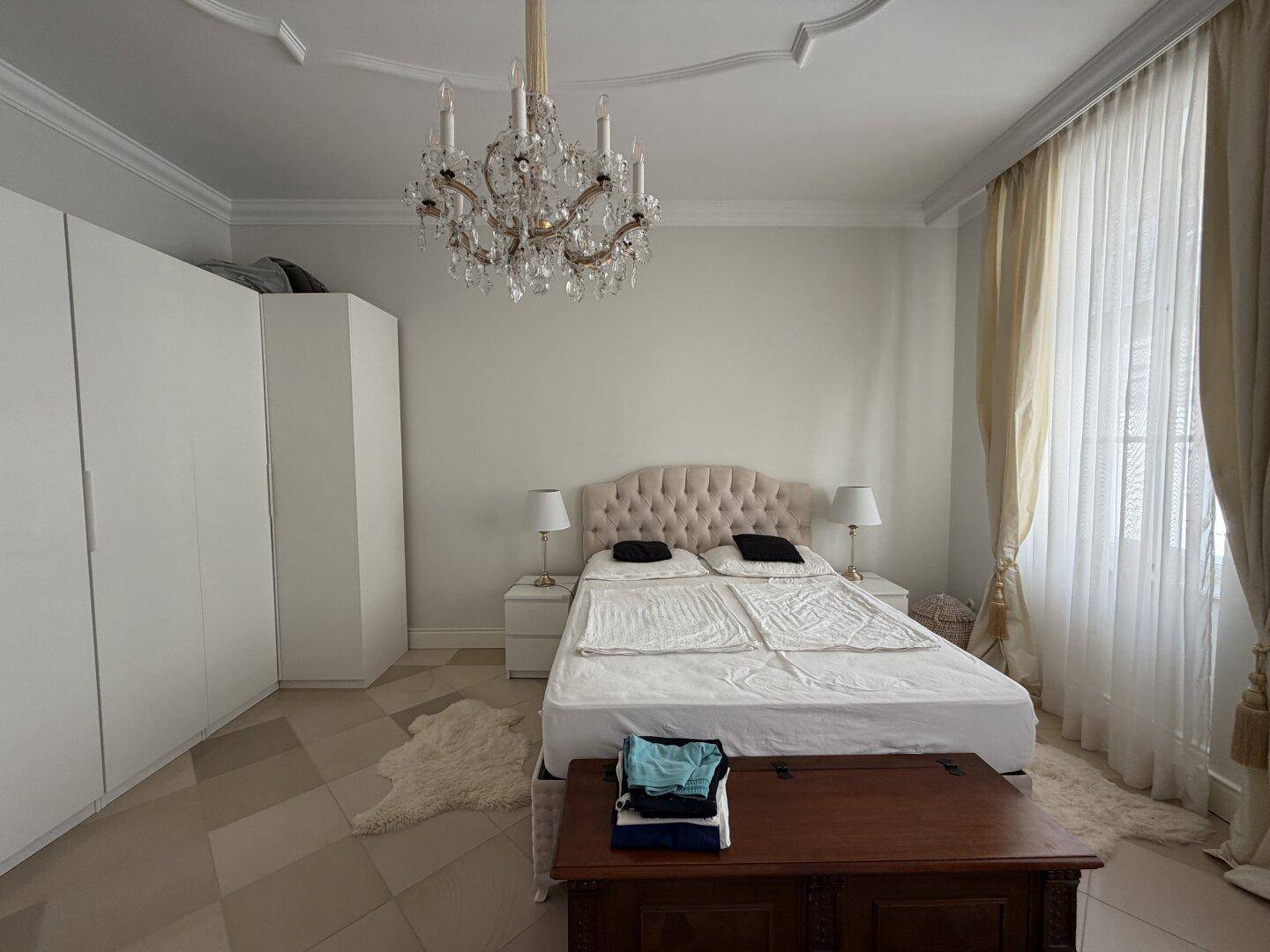 Helles Schlafzimmer mit großem Bett, weißen Schränken und Kronleuchter.