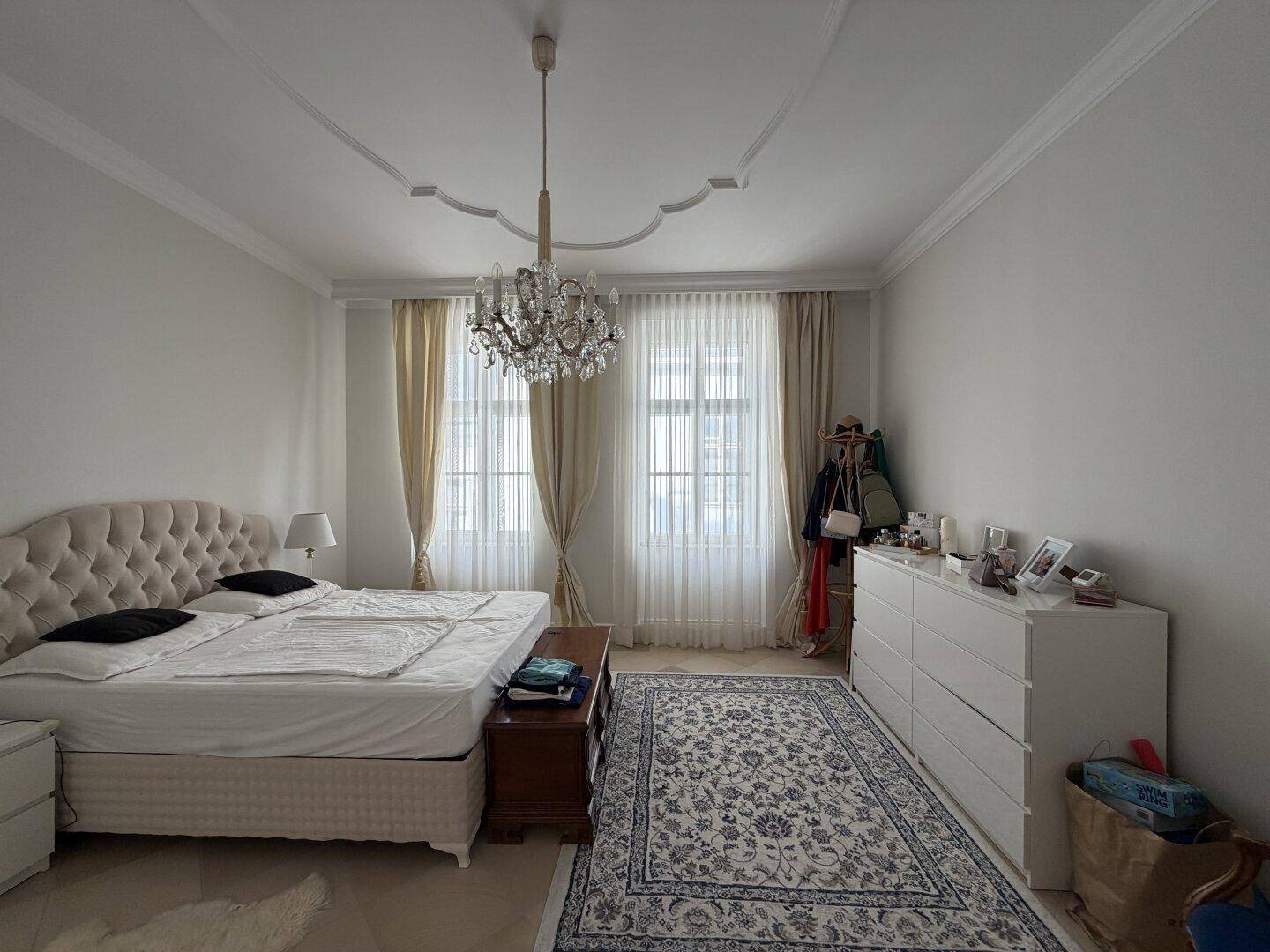 Elegantes Schlafzimmer mit Doppelbett, gemustertem Teppich und Kronleuchter.