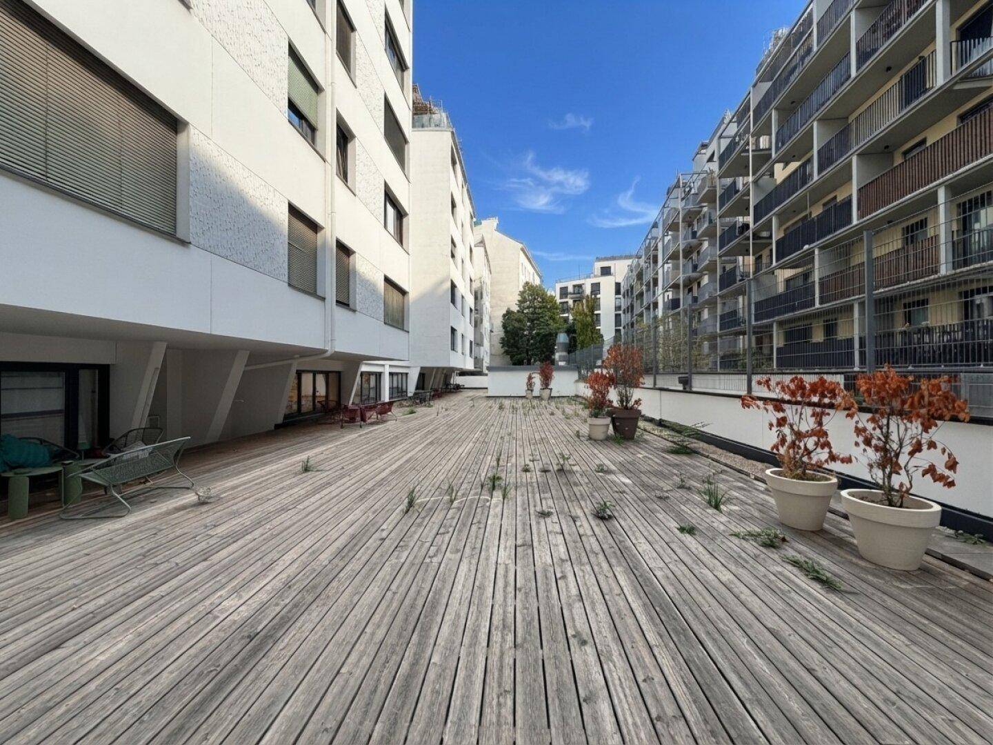 Große Holzterrasse zwischen modernen Gebäuden, ideal für Entspannung im Freien.