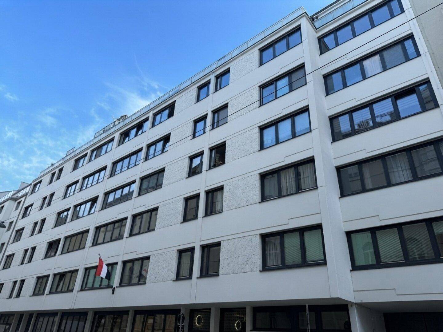 Moderne Fassade eines Mehrfamilienhauses mit zahlreichen Fenstern unter blauem Himmel.