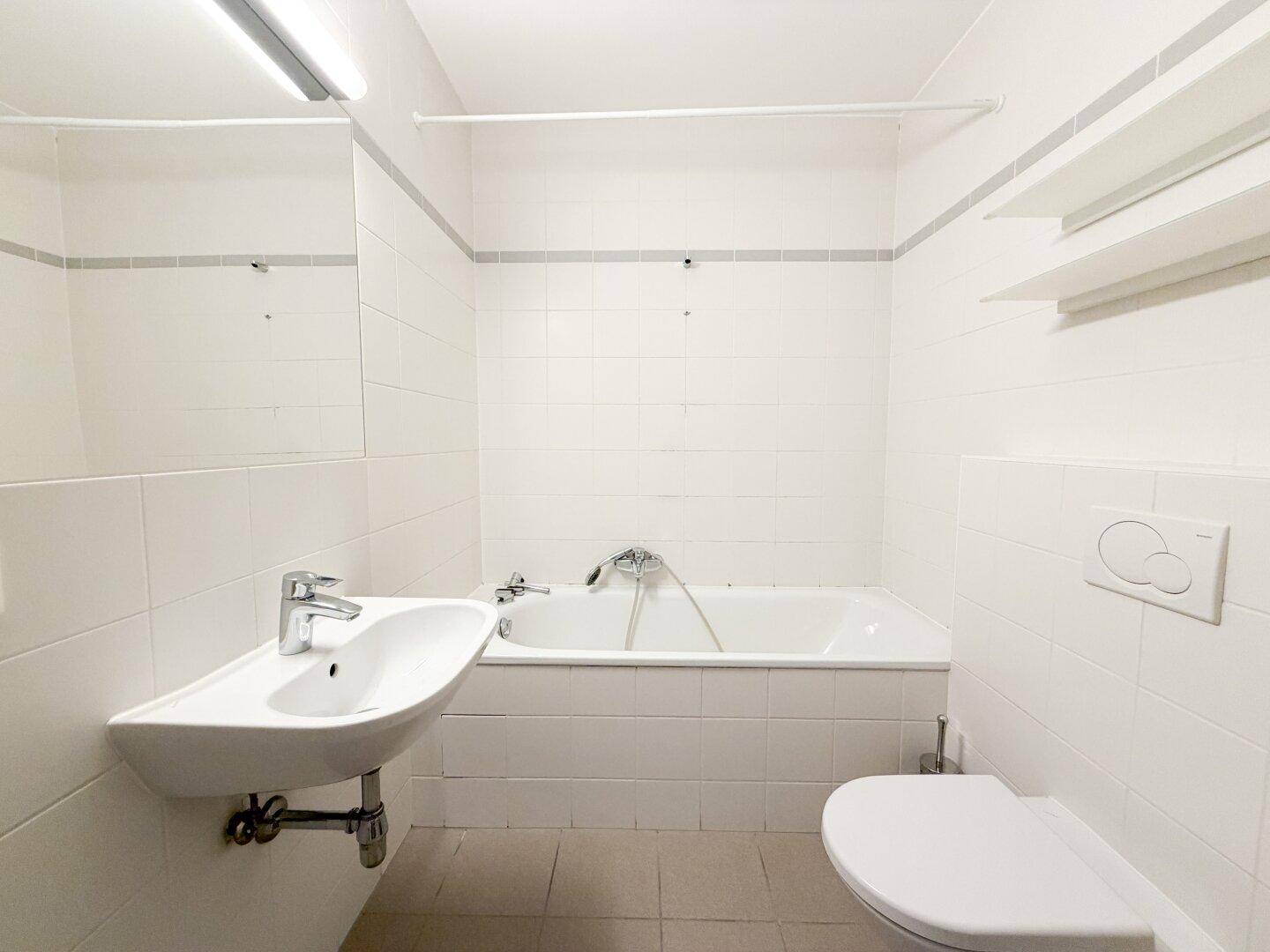 Helles Badezimmer mit weißen Fliesen, Badewanne, Waschbecken und wandhängendem WC.