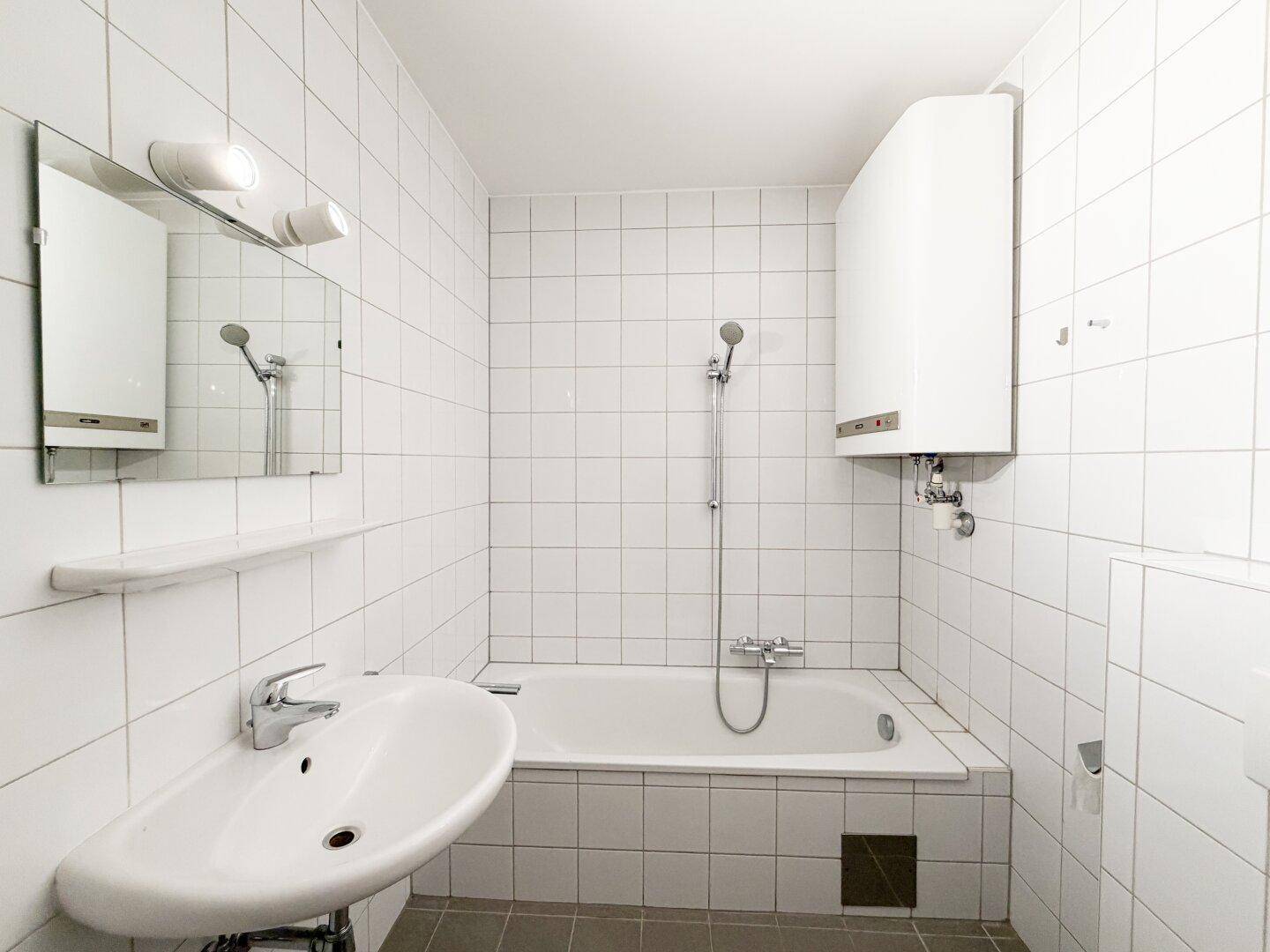 Funktionales Badezimmer mit Badewanne, Waschbecken und weißen Fliesen, inklusive Warmwasserboiler.
