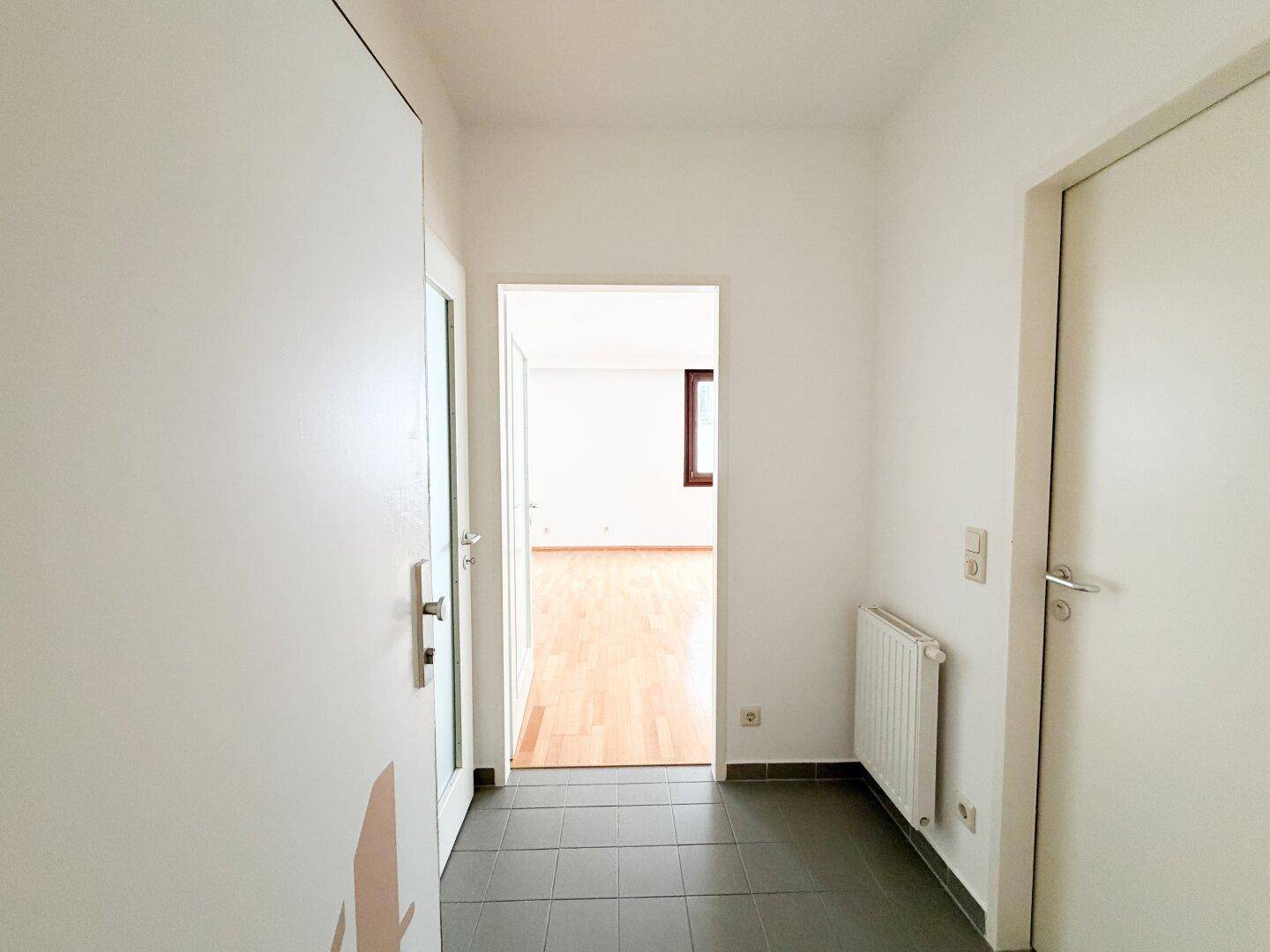Heller Flur mit Fliesenboden und Zugang zu verschiedenen Räumen, inklusive Heizkörper.