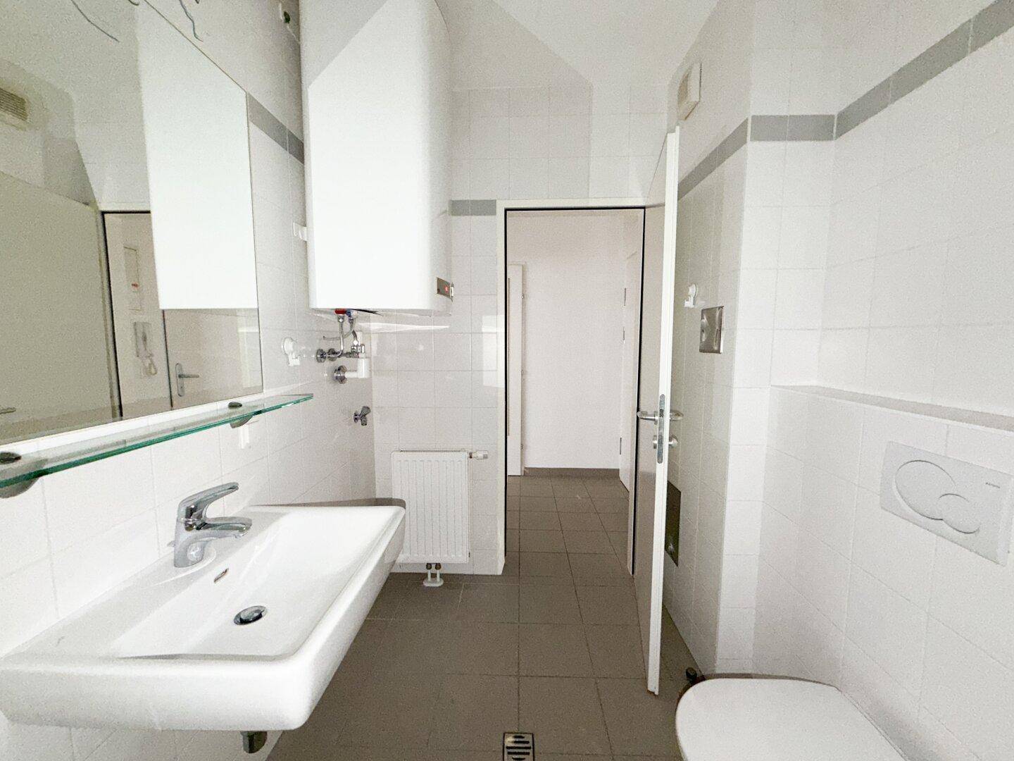 Gepflegtes Badezimmer mit Waschbecken, WC und Wandboiler, durch eine Tür zugänglich.