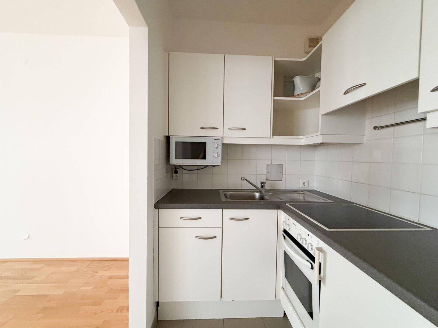 Kompakte Einbauküche mit weißen Schränken, Mikrowelle und Herd, praktisch und funktional.