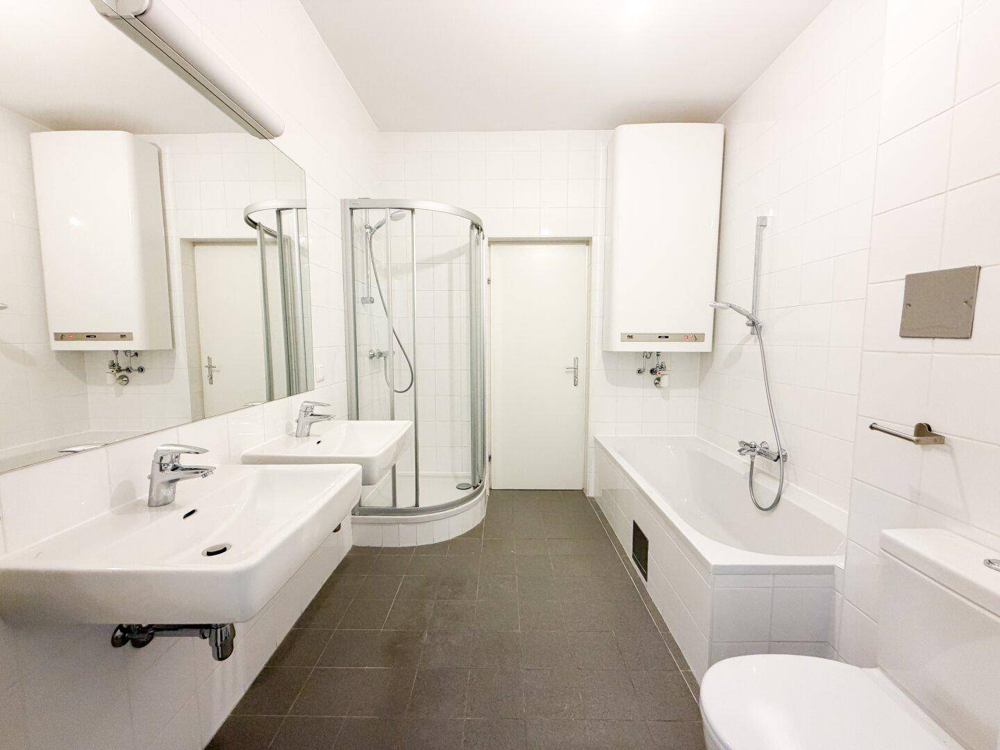 Helles Badezimmer mit Doppelwaschbecken, Badewanne und Duschkabine.