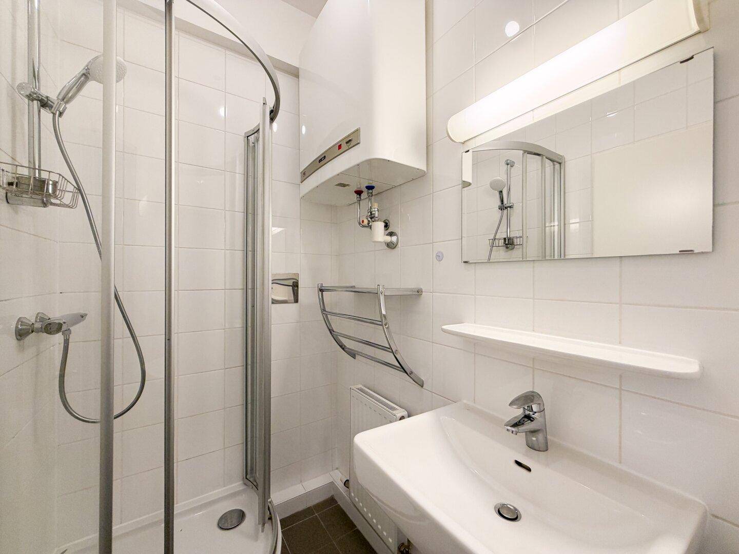 Kleines Badezimmer mit Duschkabine, Waschbecken und Boiler.