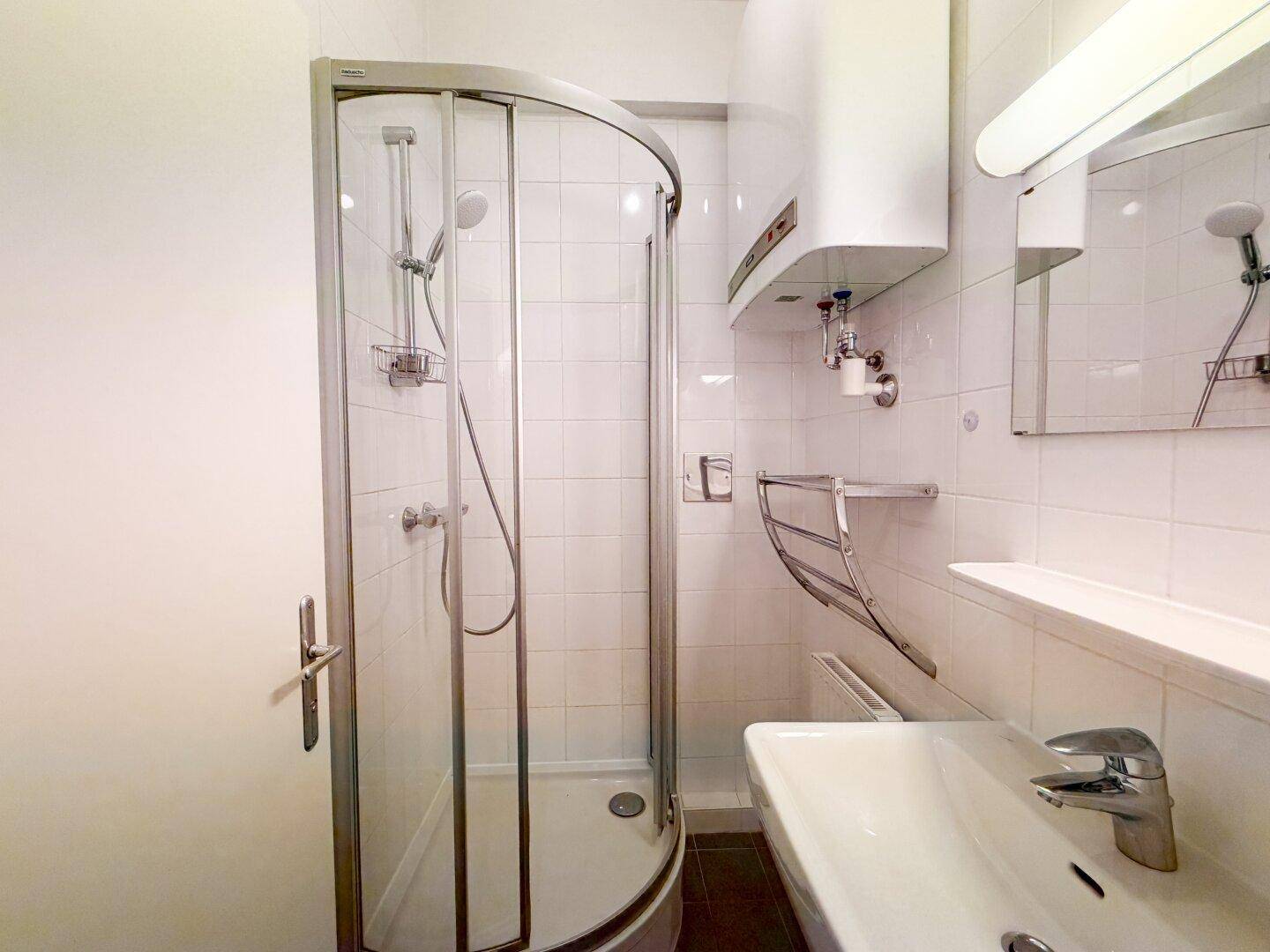 Funktionales Badezimmer mit Duschkabine, Waschbecken und Spiegel.