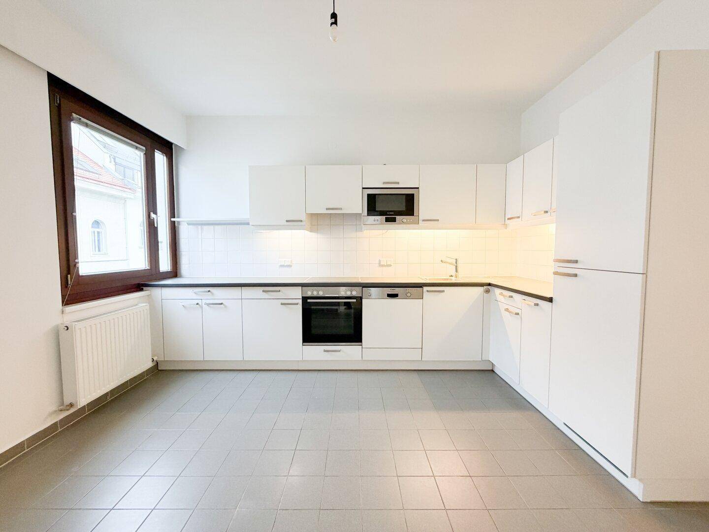Moderne Einbauküche in Weiß mit integrierten Geräten und Fliesenboden.