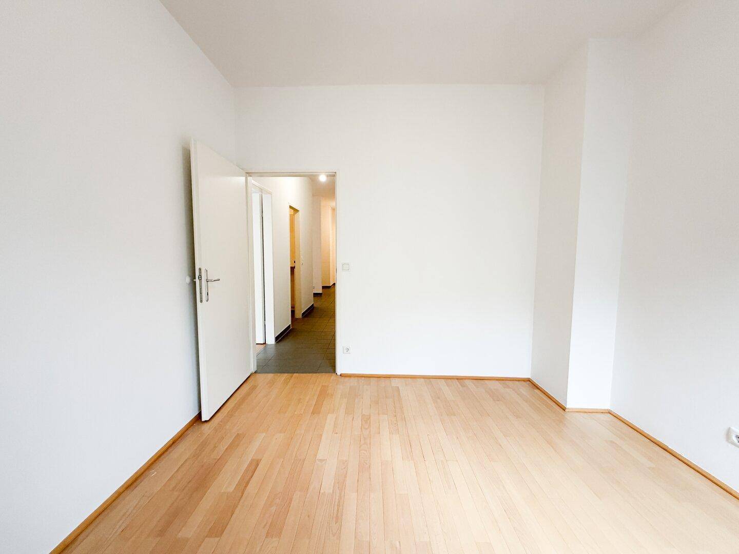 Helles Schlafzimmer mit Parkettboden und Zugang zu einem Flur.