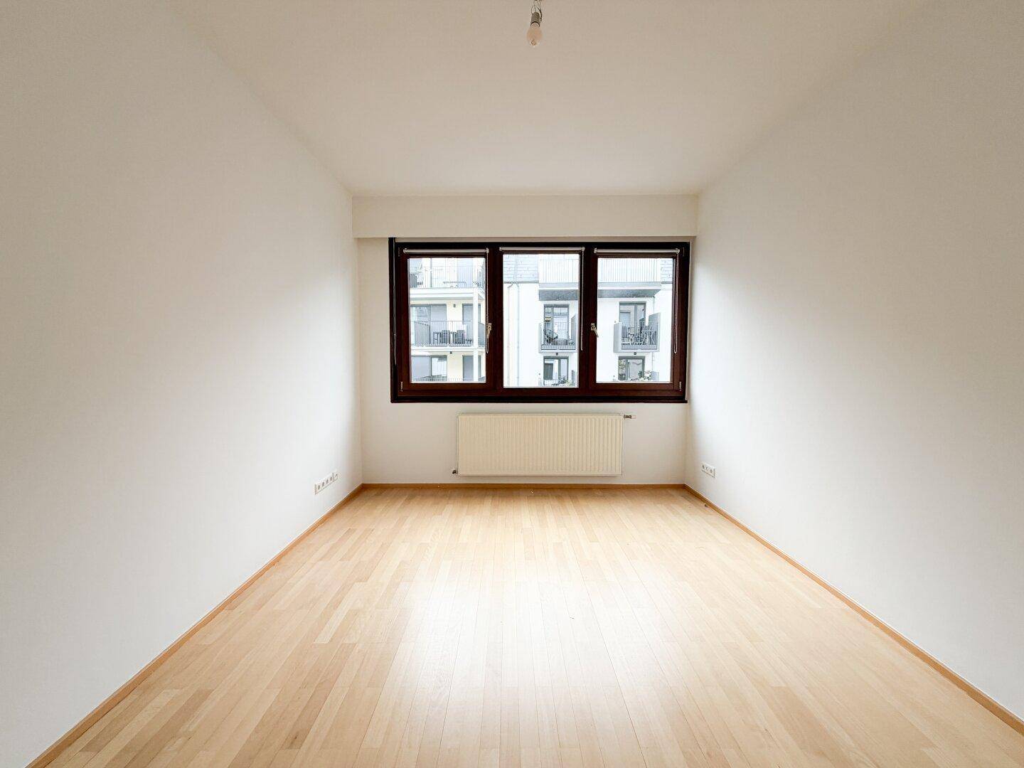 Helles, unmöbliertes Schlafzimmer mit Parkettboden und Fensterblick auf die Umgebung.