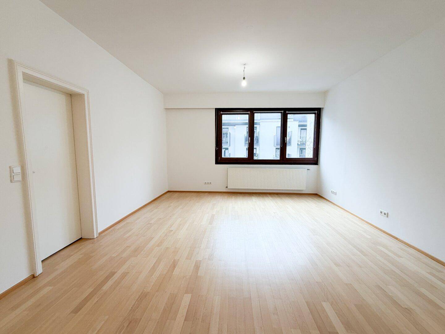 Helles Schlafzimmer mit Parkettboden und großem Fenster, unmöbliert.