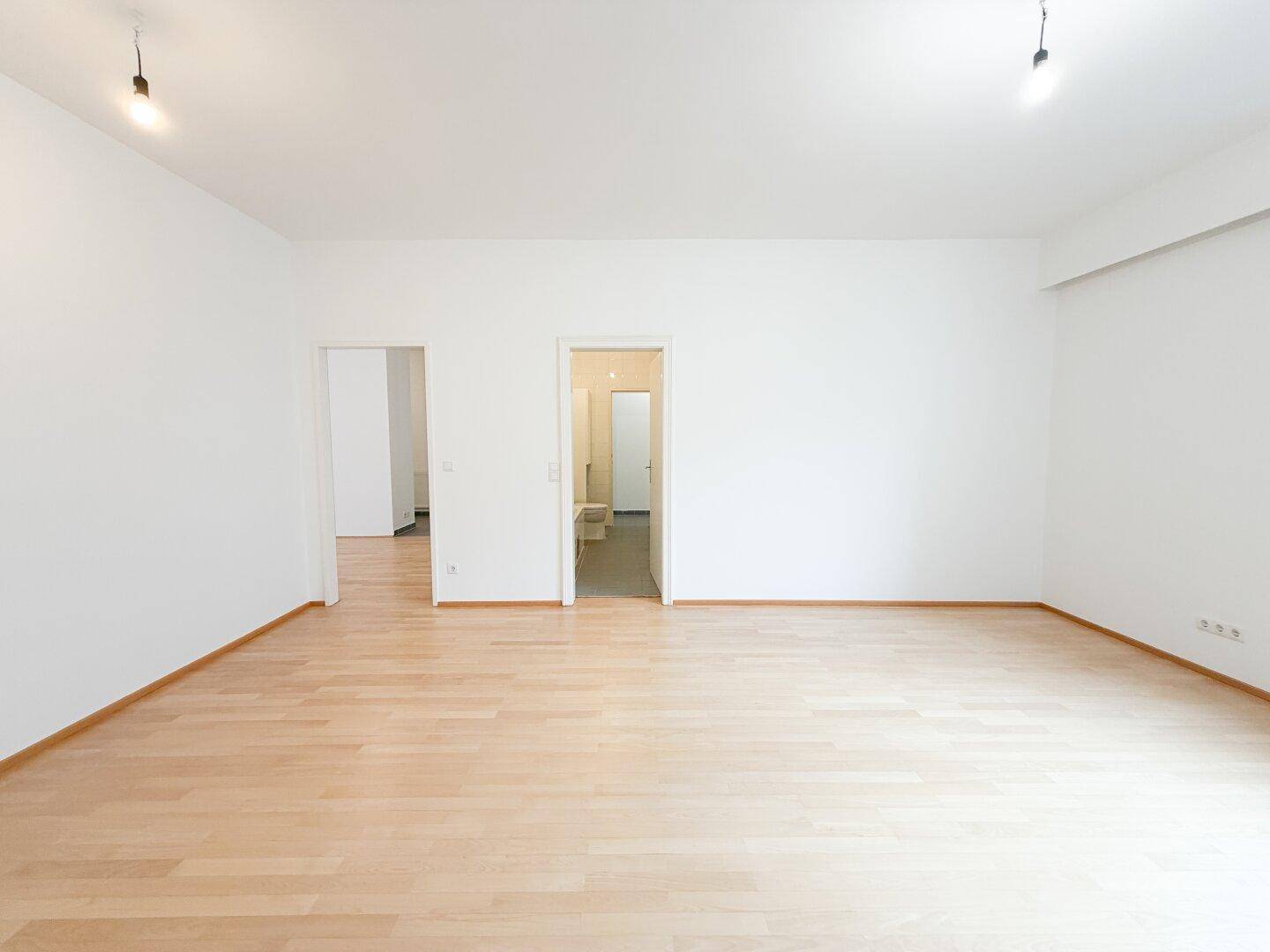 Geräumiges, unmöbliertes Schlafzimmer mit hellem Parkettboden und Zugang zu weiteren Räumen.
