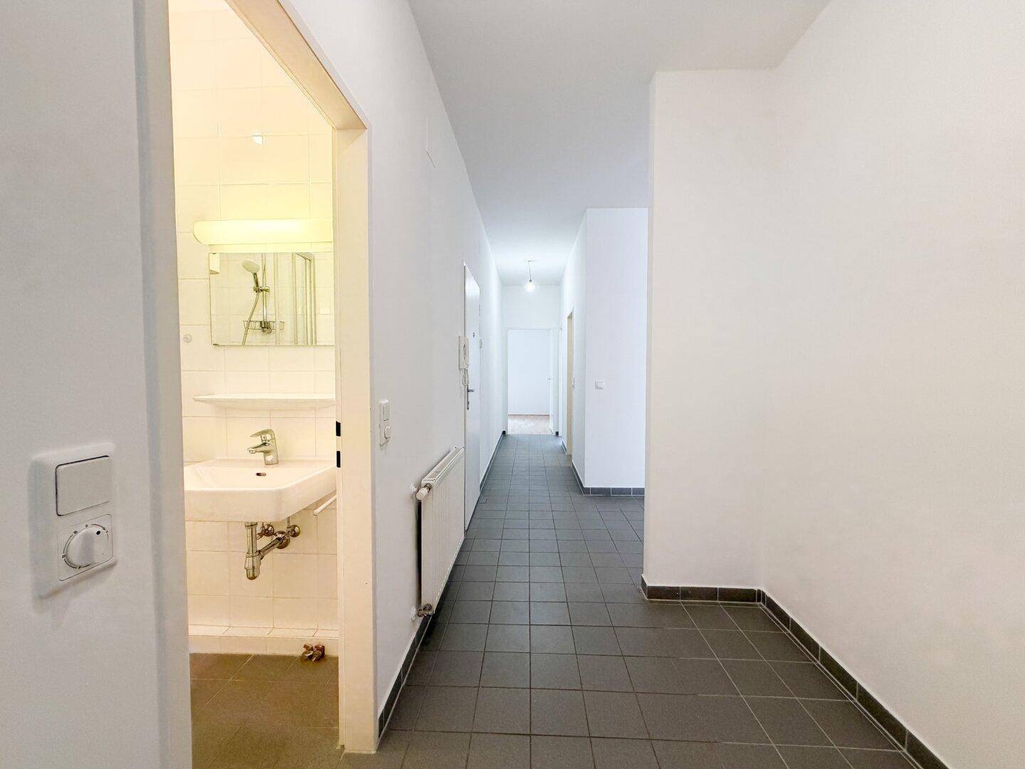 Langer Flur mit Fliesenboden und Zugang zu einem Badezimmer.