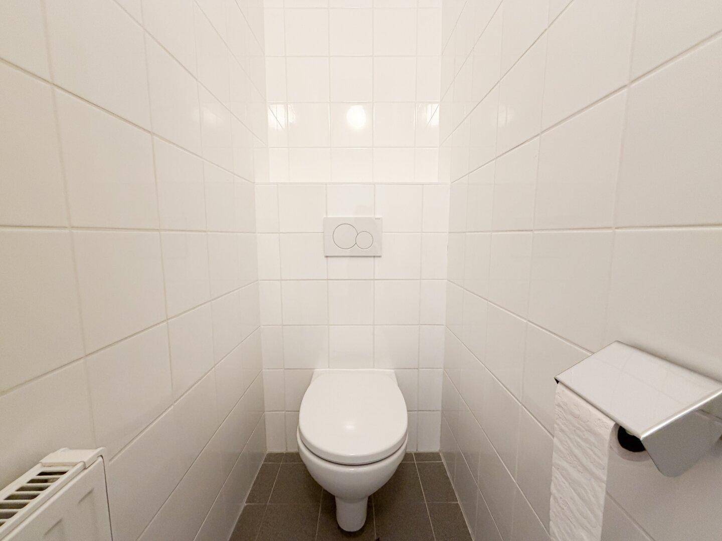 Separate Toilette mit weißen Fliesen und Wand-WC.