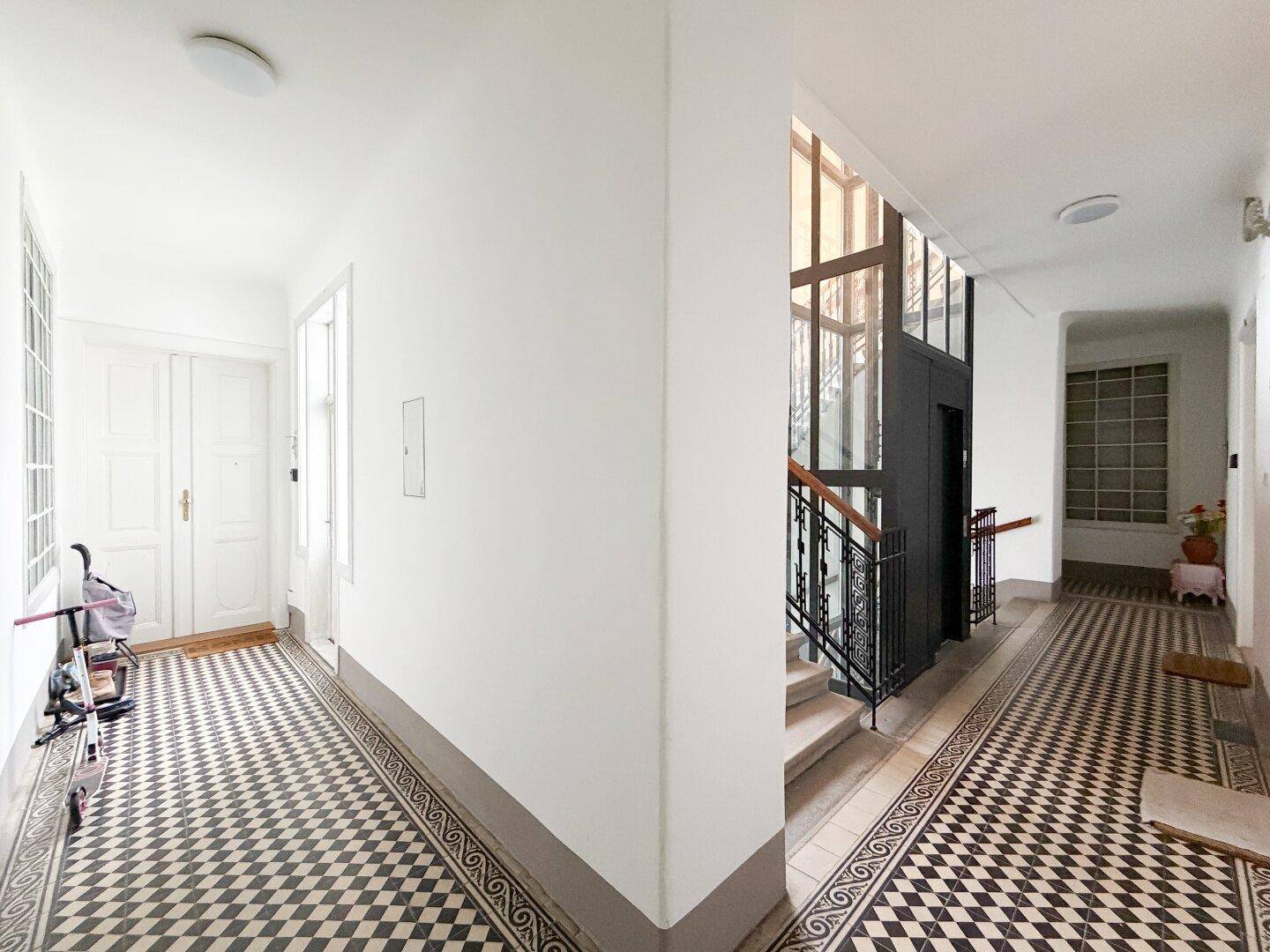 Heller Hausflur mit gemusterten Fliesen und einem modernen Glasaufzug neben der Treppe.