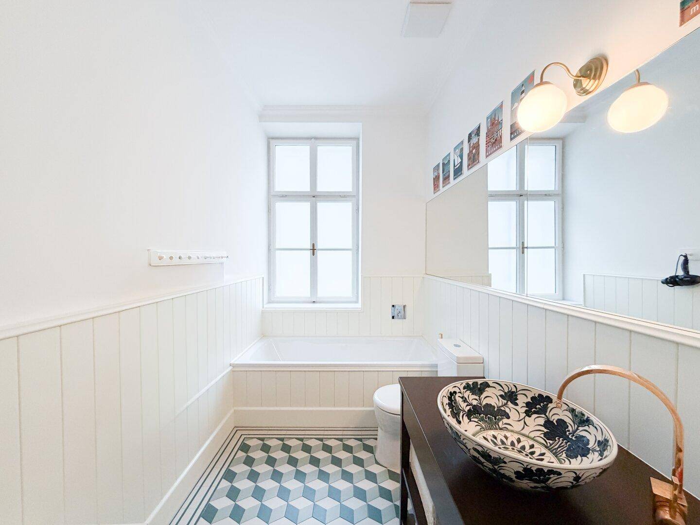 Helles Badezimmer mit Badewanne, WC, stilvollem Waschbecken und auffälligen Bodenfliesen.