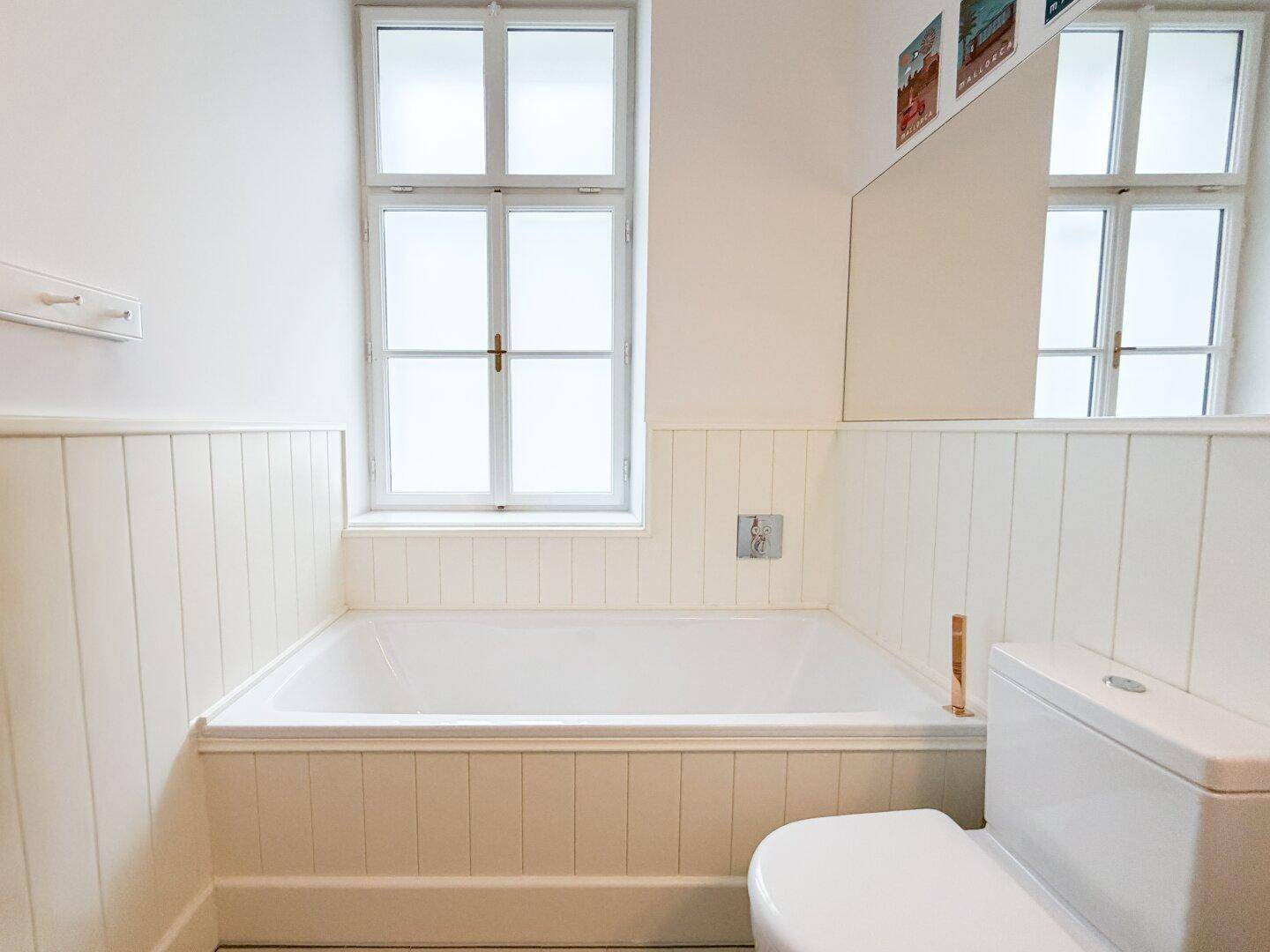 Badezimmer mit eingebauter Badewanne, Toilette und weißer Holzverkleidung an den Wänden.