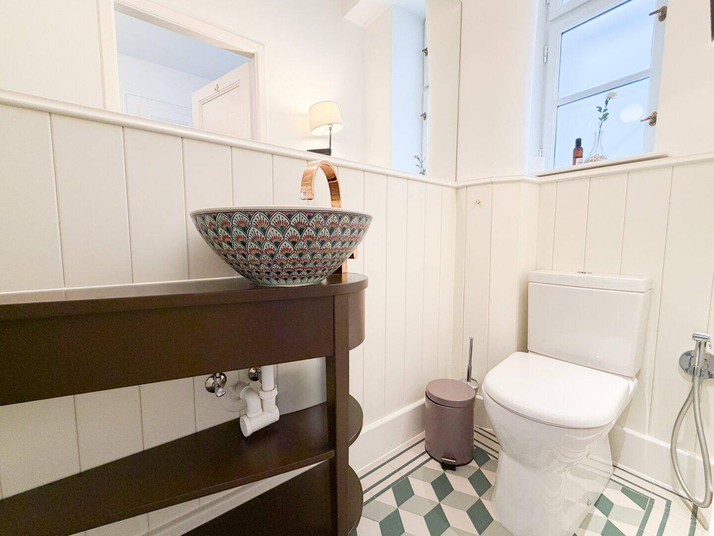 Helles Badezimmer mit stilvollem Waschbecken, Toilette und geometrischen Bodenfliesen.