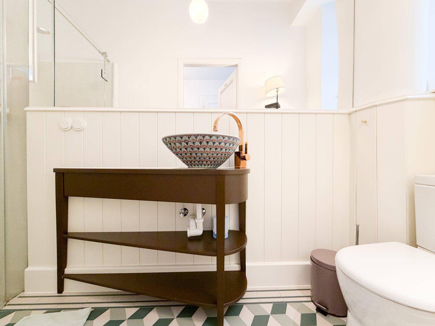 Badezimmer mit modernem Waschbecken, Toilette und einer Duschkabine im Hintergrund.