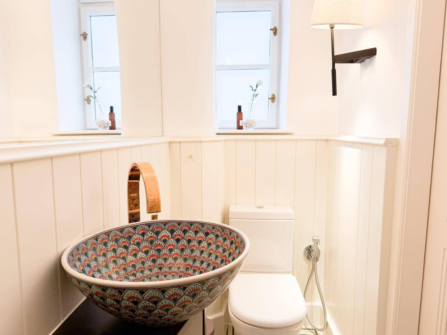 Badezimmer mit farbenfrohem Aufsatzwaschbecken, Toilette und weißer Holzverkleidung.