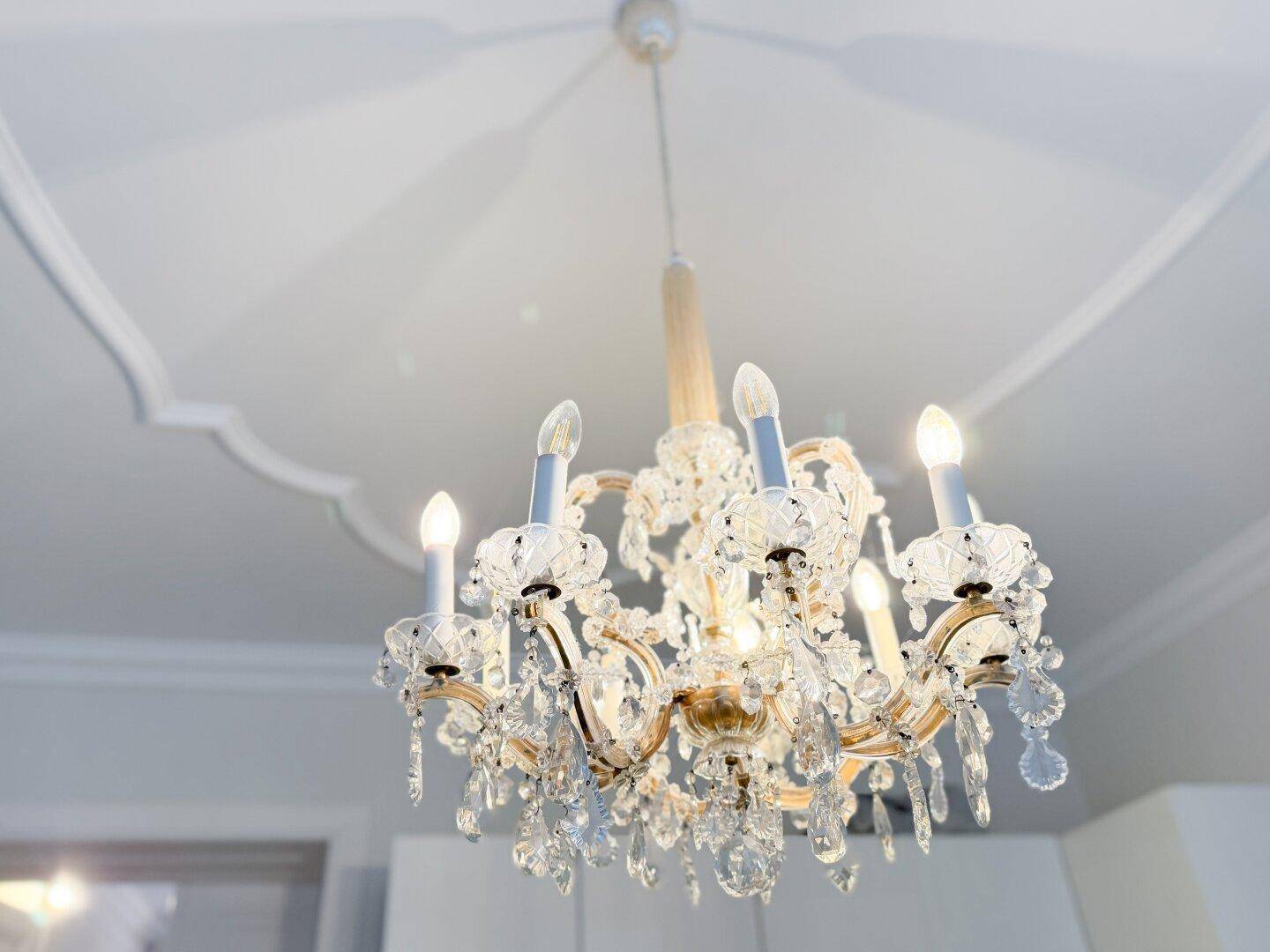 Detailansicht eines glitzernden Kronleuchters mit Kristallbehängen und klassischer Deckenrosette.
