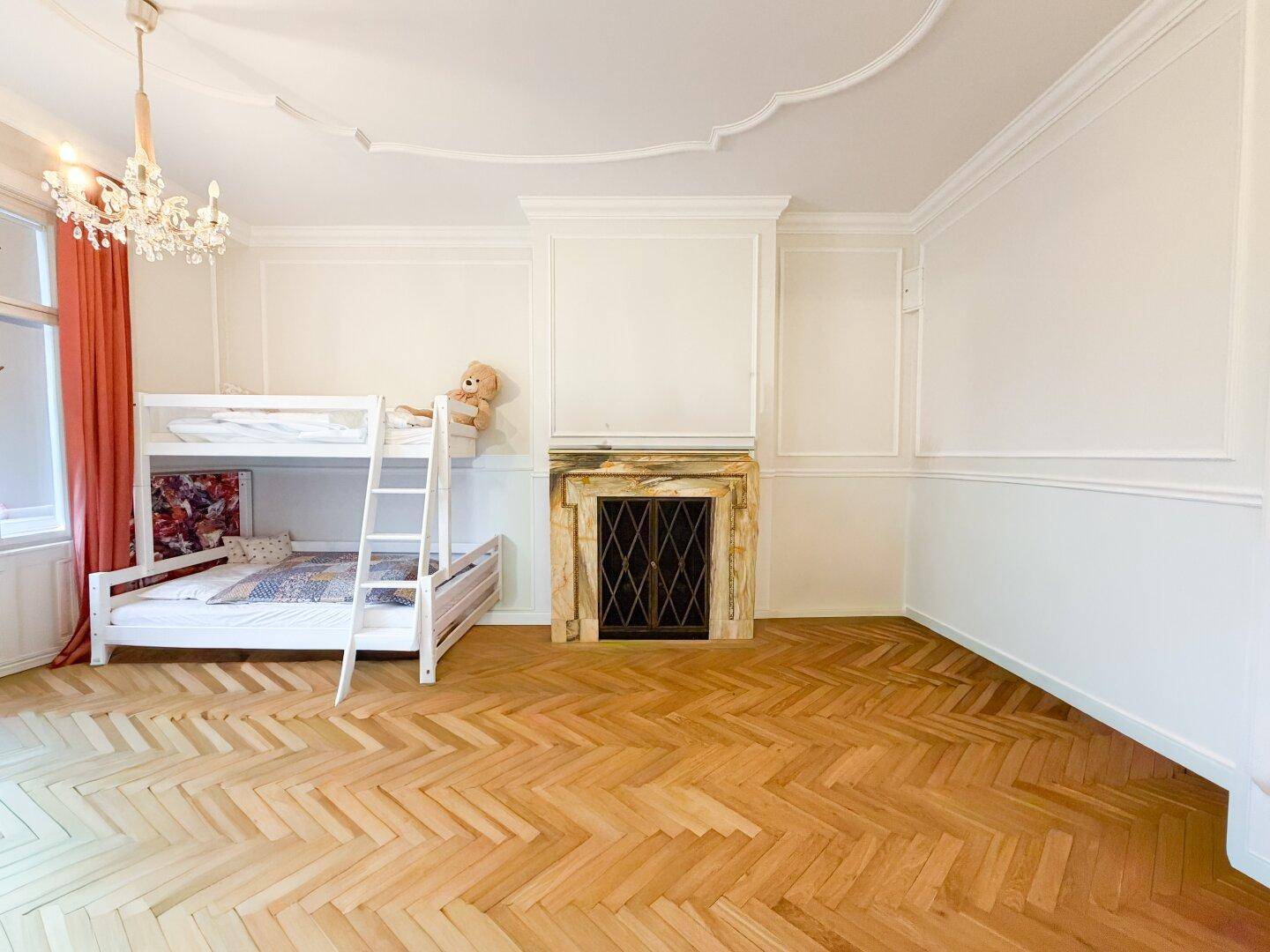 Helles Kinderzimmer mit Etagenbett, klassischem Kamin und Fischgrätparkettboden.