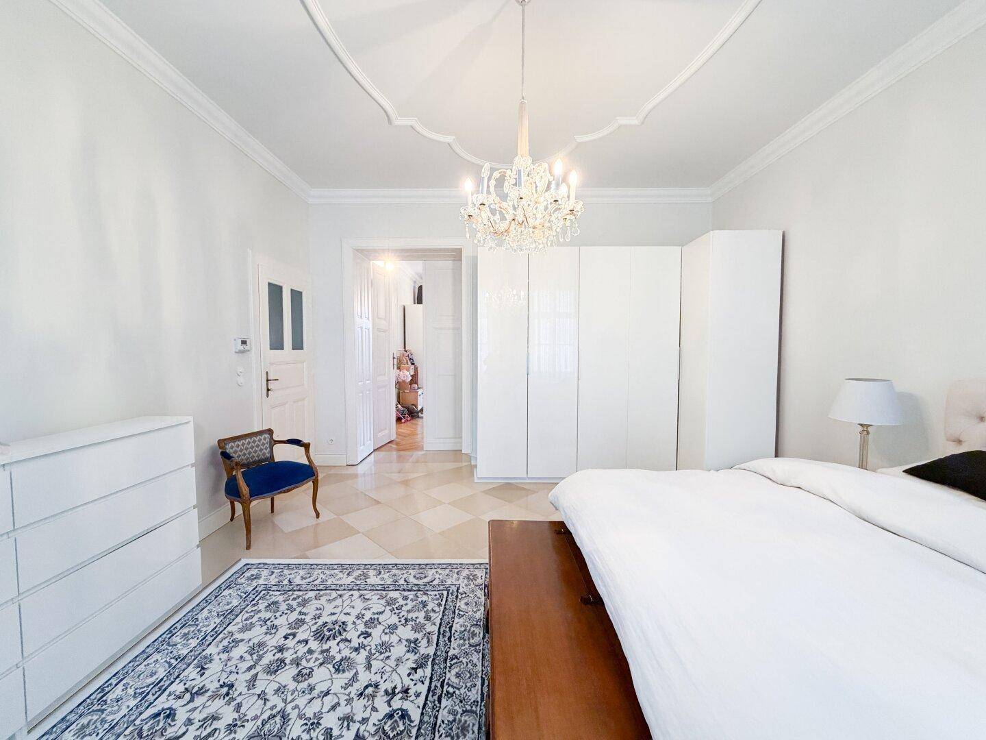 Schlafzimmer mit weißem Kleiderschrank, elegantem Bett und Blick in den angrenzenden Flur.