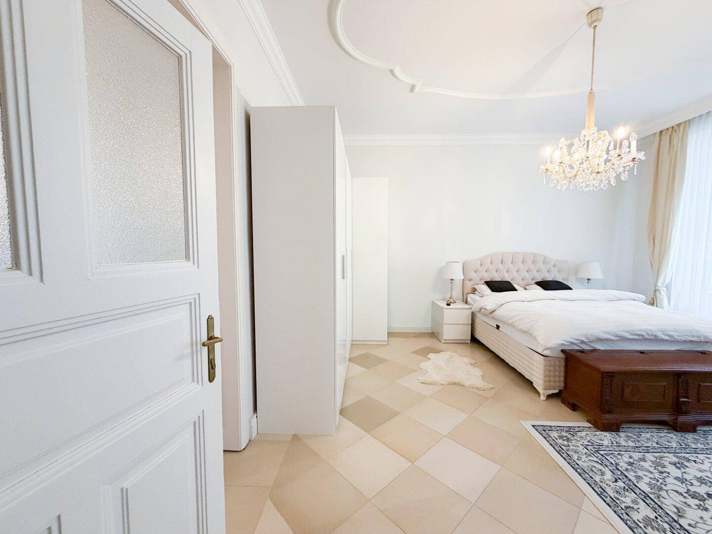 Helles Schlafzimmer mit weißem Kleiderschrank, elegantem Bett und gemusterten Bodenfliesen.