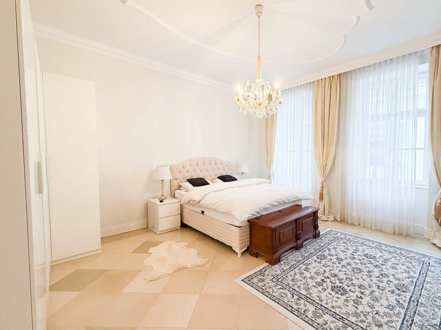 Elegantes Schlafzimmer mit großem Bett, Kronleuchter und hellen Fliesen im Schachbrettmuster.