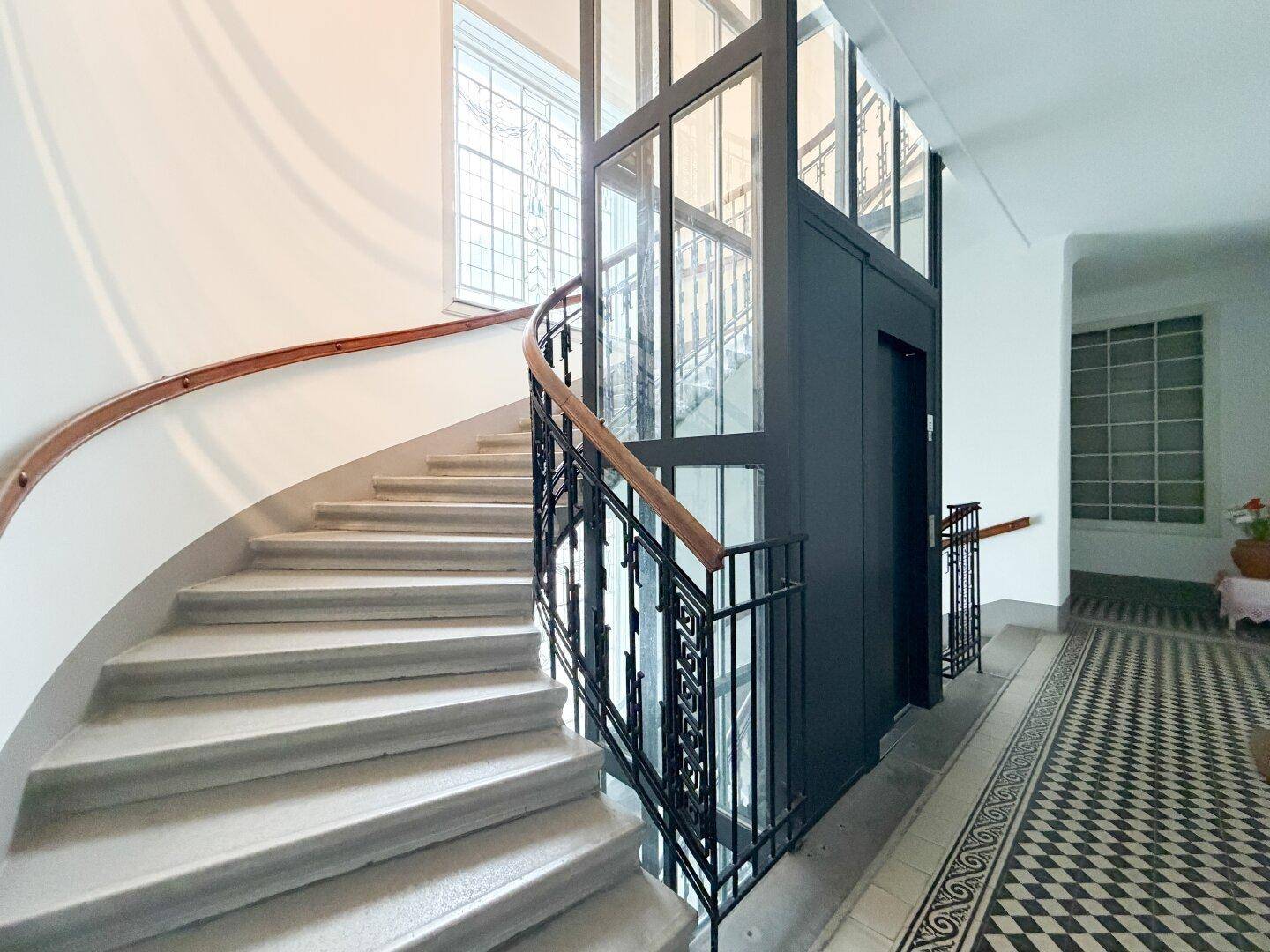 Detailansicht des modernen Glasaufzugs und der geschwungenen Treppe im eleganten Treppenhaus.