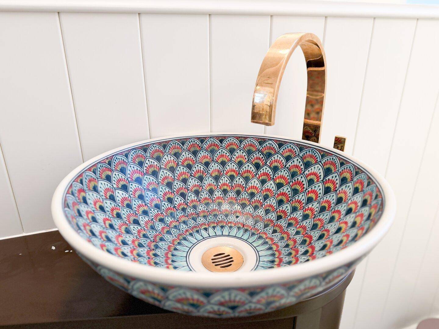 Nahaufnahme eines weiteren farbenfroh gemusterten Waschbeckens mit einem modernen goldenen Wasserhahn.