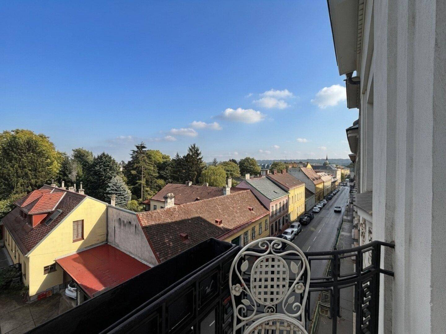 Balkon mit schmiedeeisernem Geländer und Blick auf eine ruhige Wohnstraße mit Bäumen.