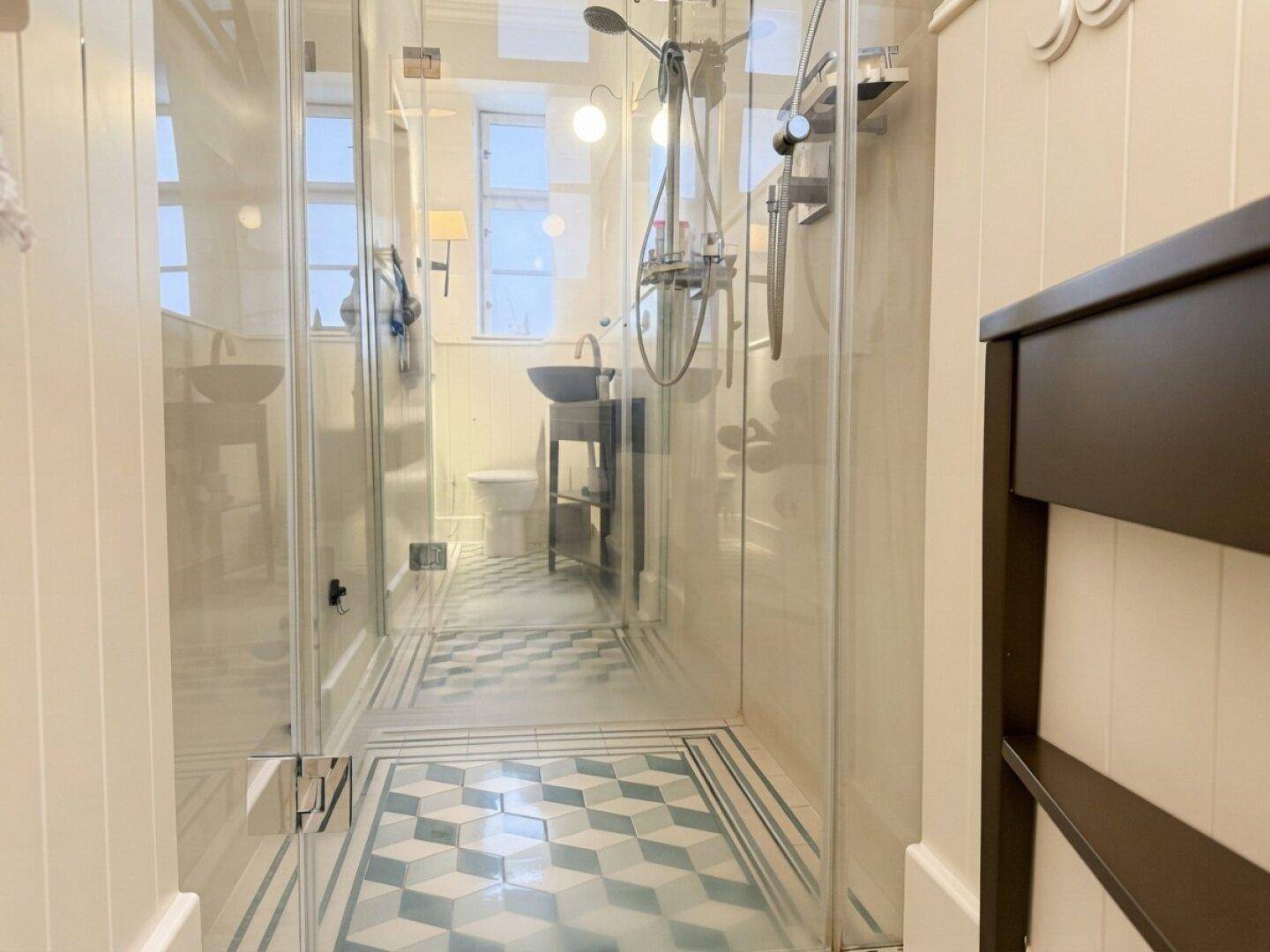 Geräumige begehbare Dusche mit Glasabtrennung und auffälligen geometrischen Bodenfliesen.