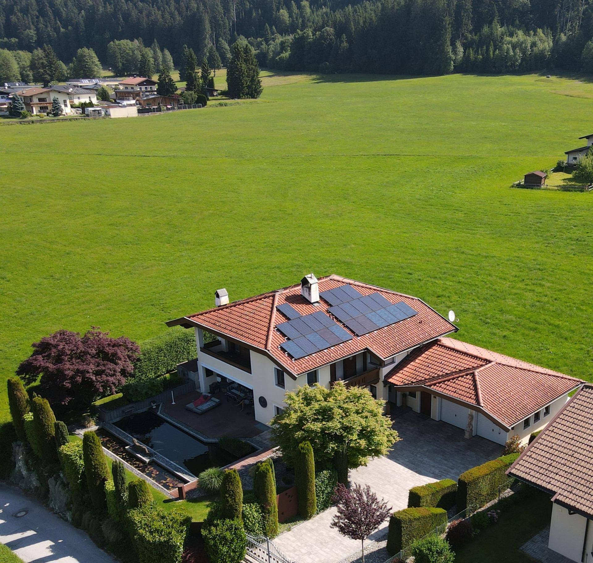 Luftaufnahme des Hauses mit Garten, Teich, Doppelgarage und Zufahrt, umgeben von grünen Wiesen.