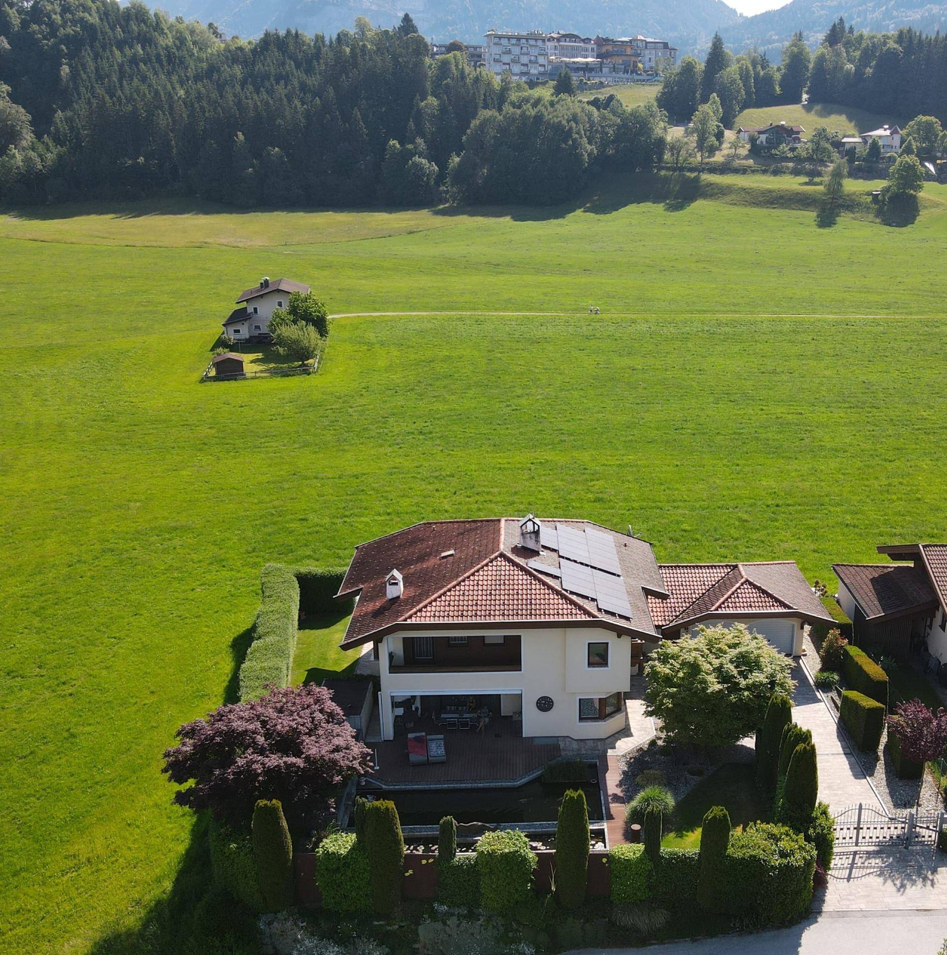 Weitläufige Luftaufnahme des Anwesens, eingebettet in grüne Wiesen mit beeindruckendem Bergpanorama.