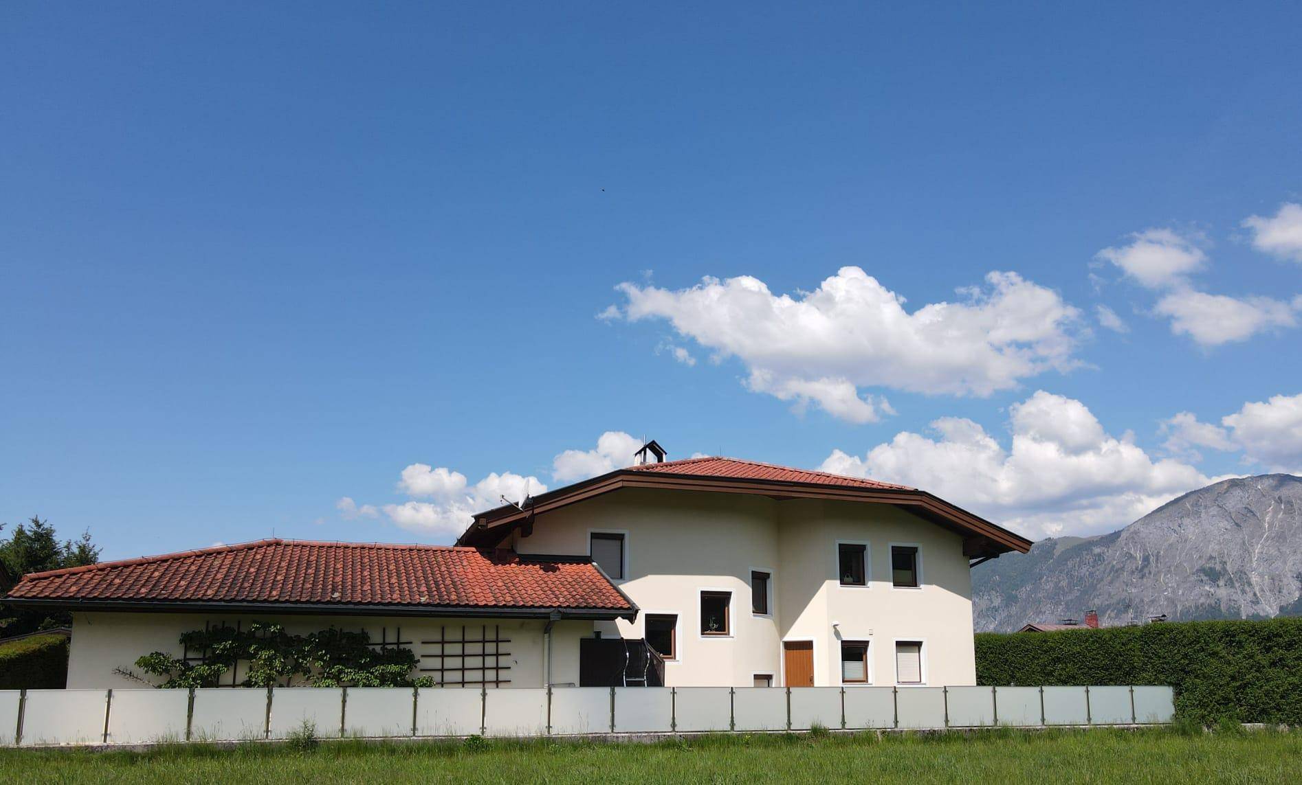 Ansicht des Hauses von der Wiese aus, mit klarer Fassade, Ziegeldach und Bergkulisse.