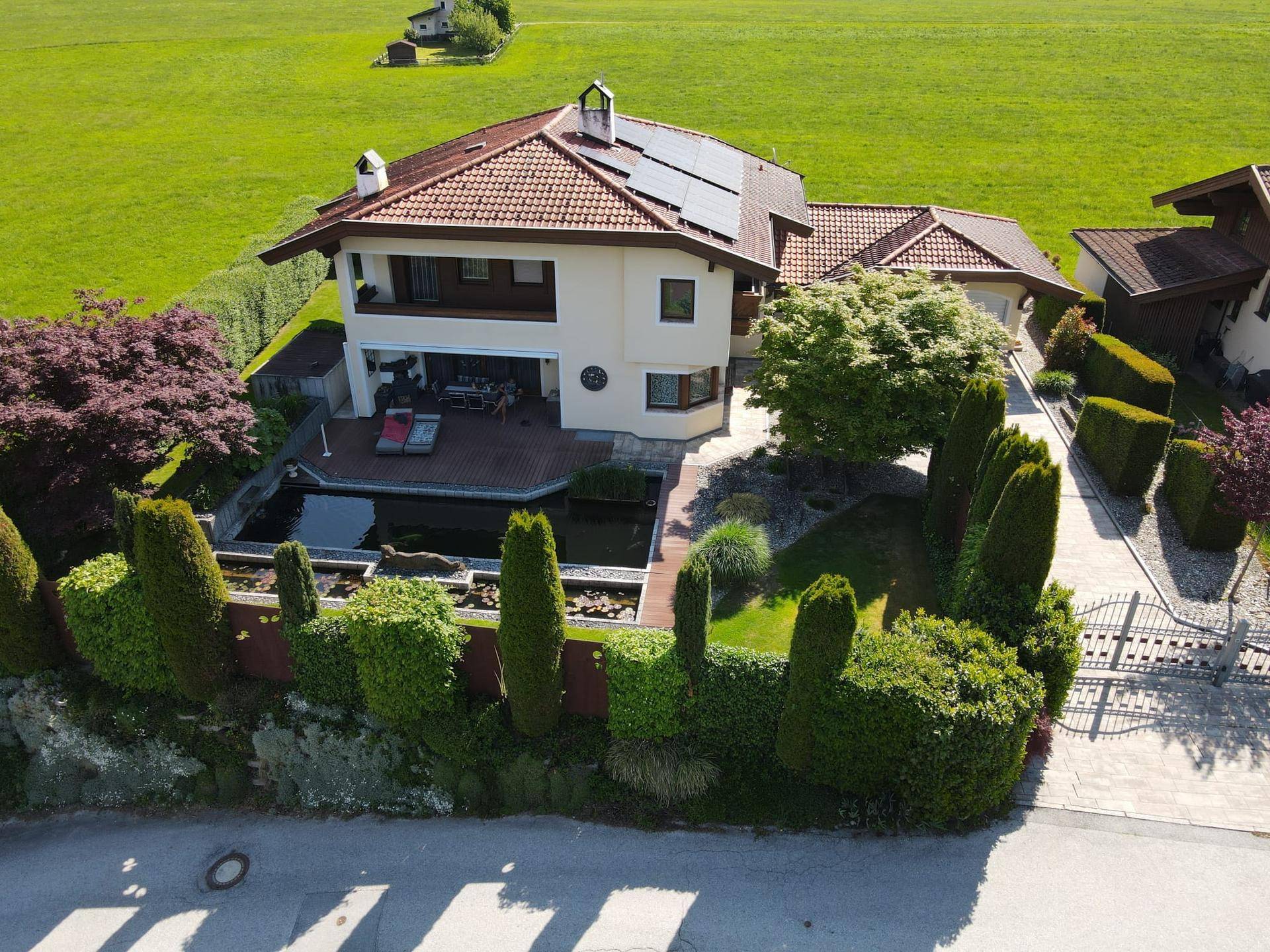 Anwesen von oben mit gepflegtem Garten, Teich, Zufahrt und Blick auf die angrenzende Straße.